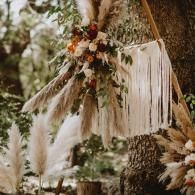 Boho floral wedding arch with pampas grass, white drapery, and orange flowers outdoors