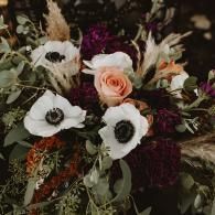 Assorted flowers in white, blush, and deep burgundy with greenery in a dark floral arrangement