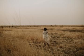Person in a white coat standing in a dry grassy field under a hazy sky