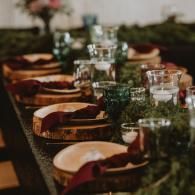Long dining table set with glassware, candles, and wooden plates in a warm, elegant setting
