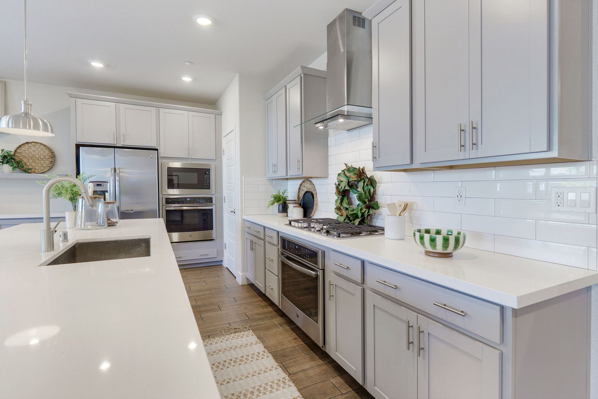 Modern kitchen with gray cabinets, white countertops, stainless steel appliances, and a central island.