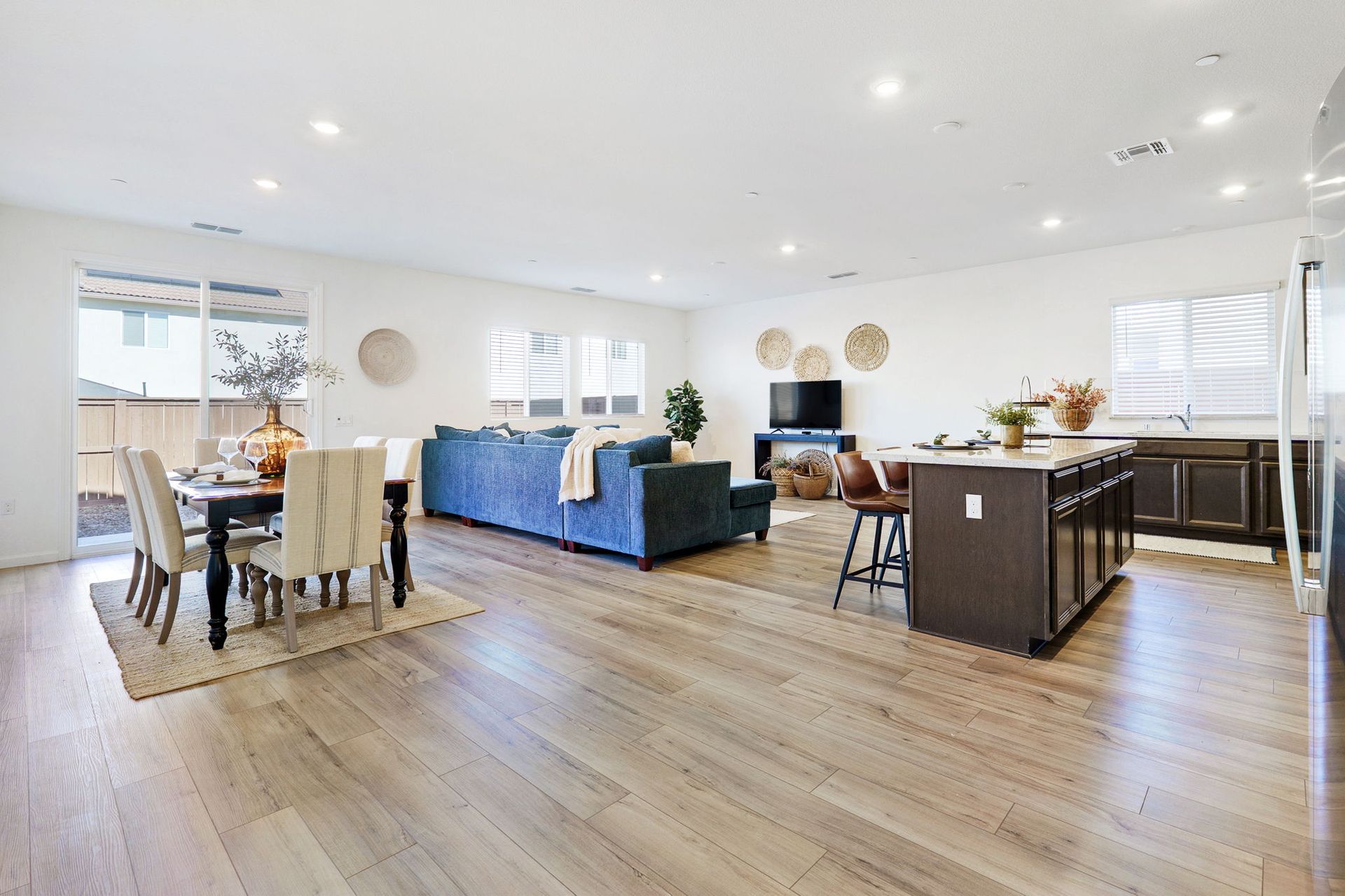Open-concept living space with dining area, kitchen island, blue sofa, and hardwood floors.