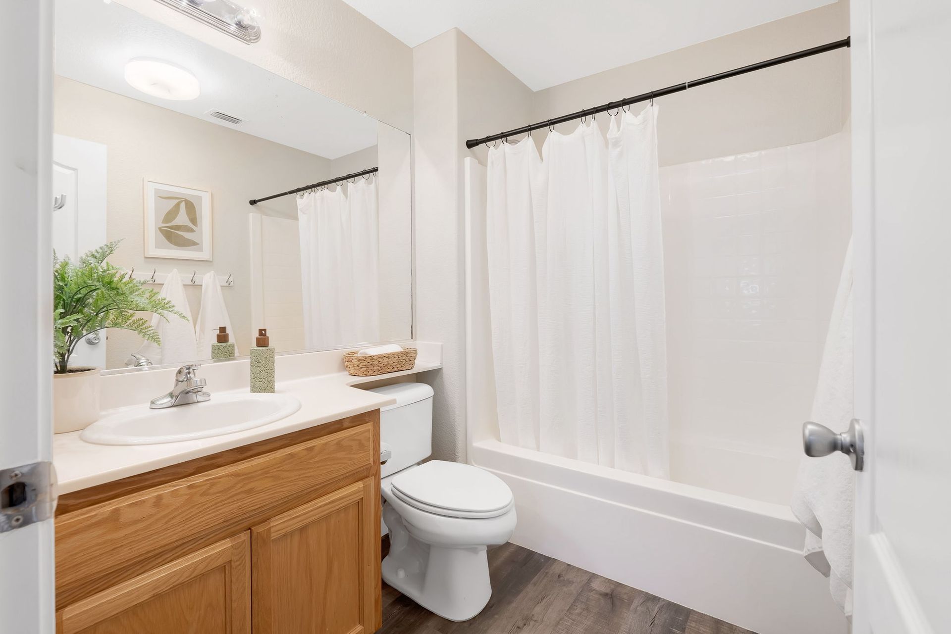 Bathroom with light wood vanity, white toilet, bathtub, and neutral decor.