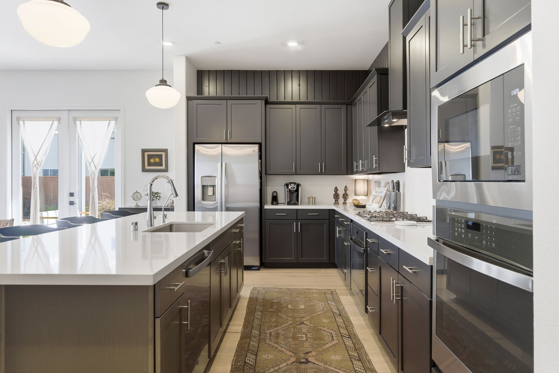 Modern kitchen with dark cabinets, stainless steel appliances, and large island with a white countertop.