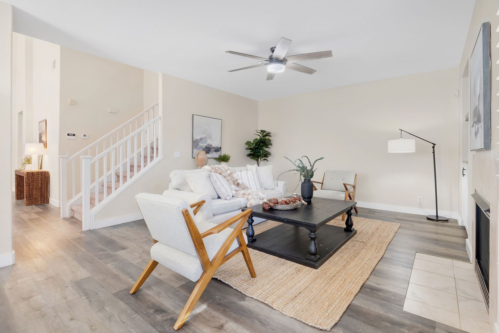 Living room with white walls, stairs, gray wood floors, and neutral-colored furniture.