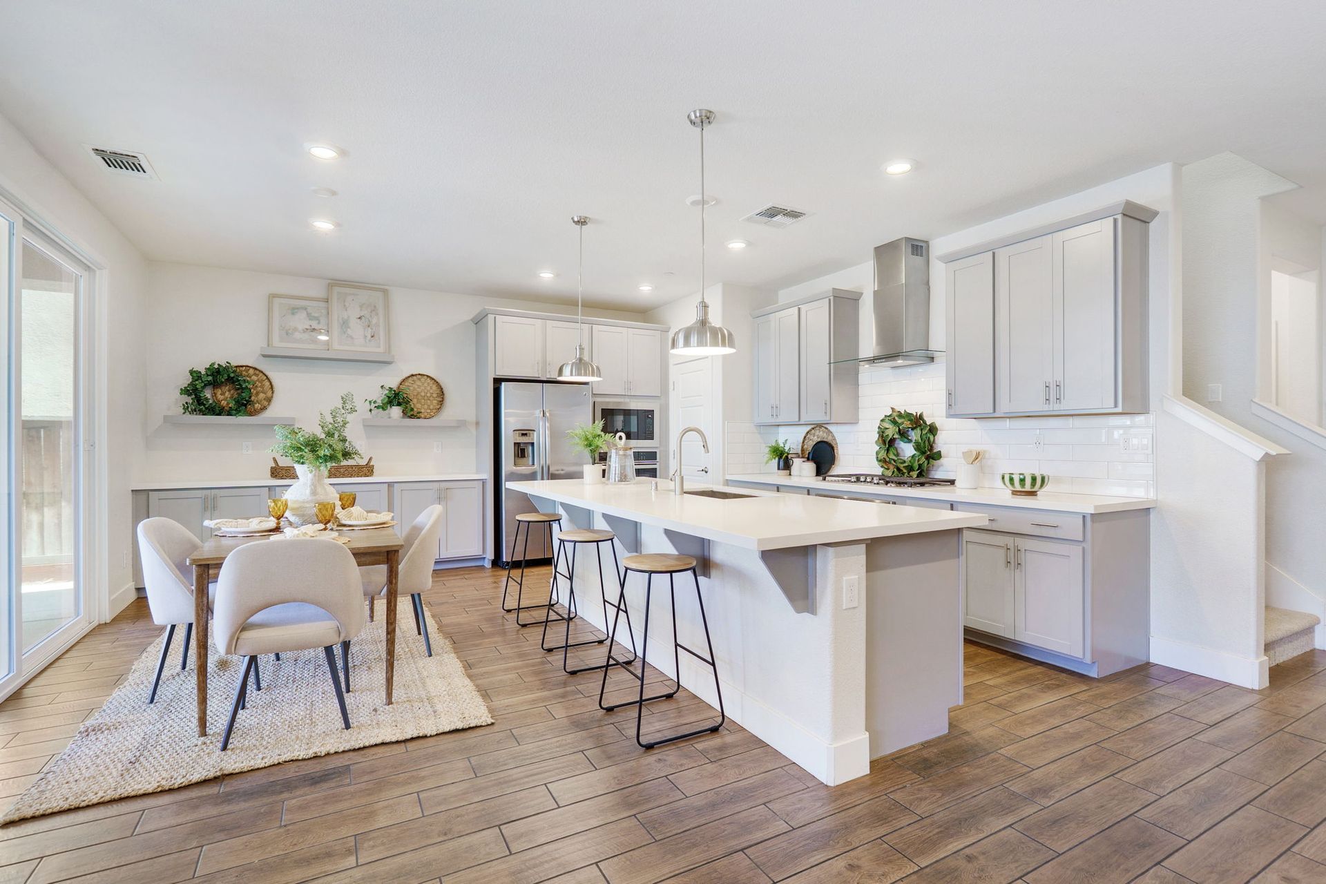 Modern kitchen with island, dining area, light gray cabinets, and hardwood floors.