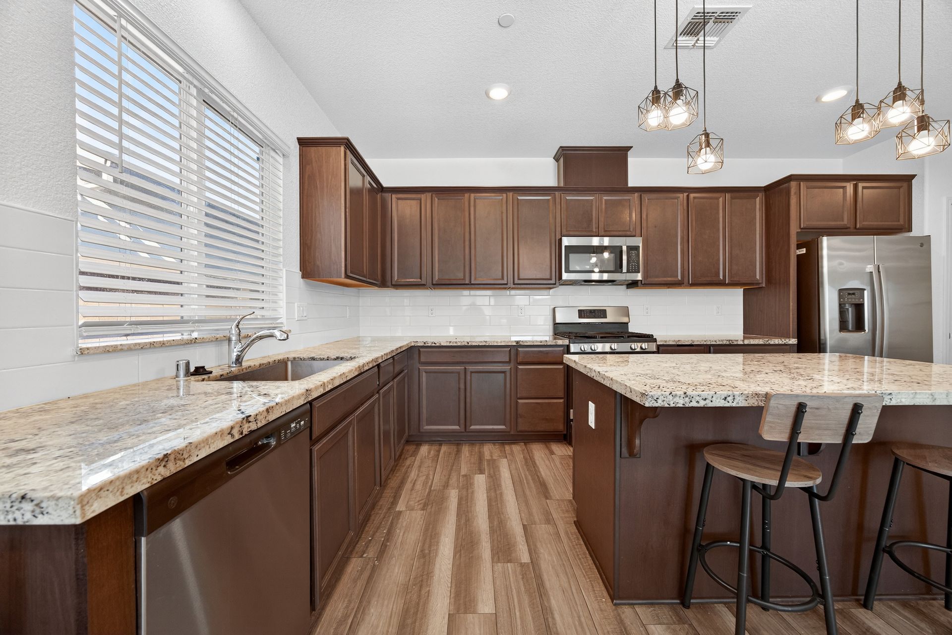 Modern kitchen with brown cabinets, stainless steel appliances, and a granite countertop island.