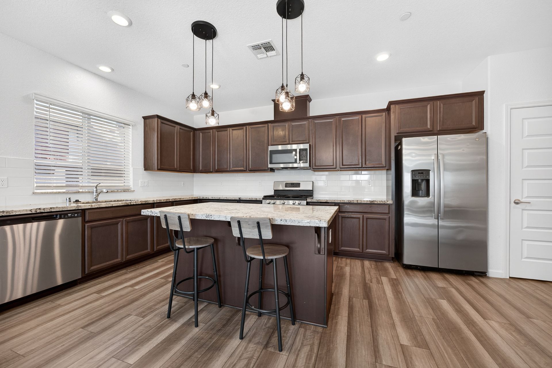 Modern kitchen with brown cabinets, stainless steel appliances, and a granite island with stools.