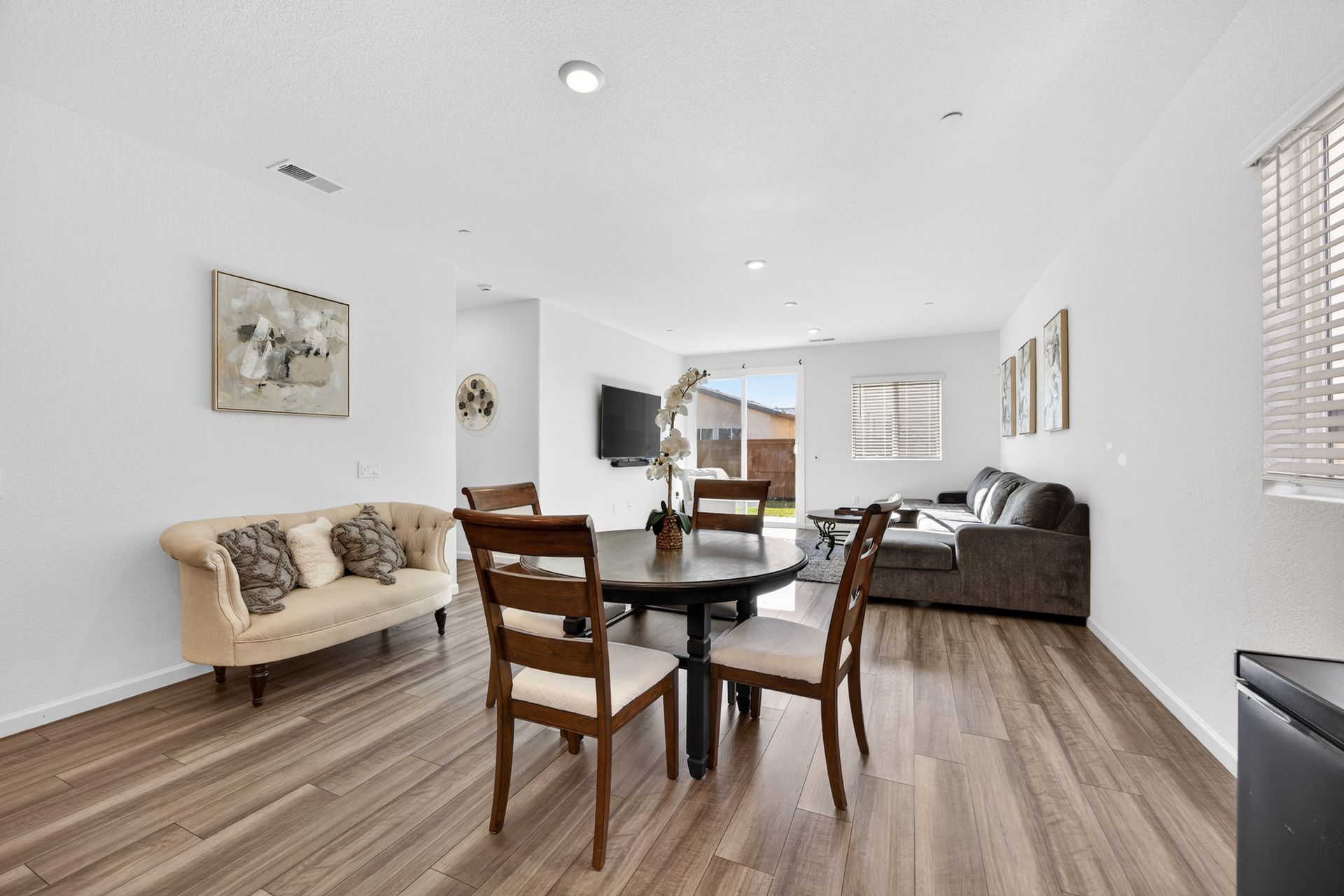 Living room with wood flooring, dining table and chairs, sofa, and television.