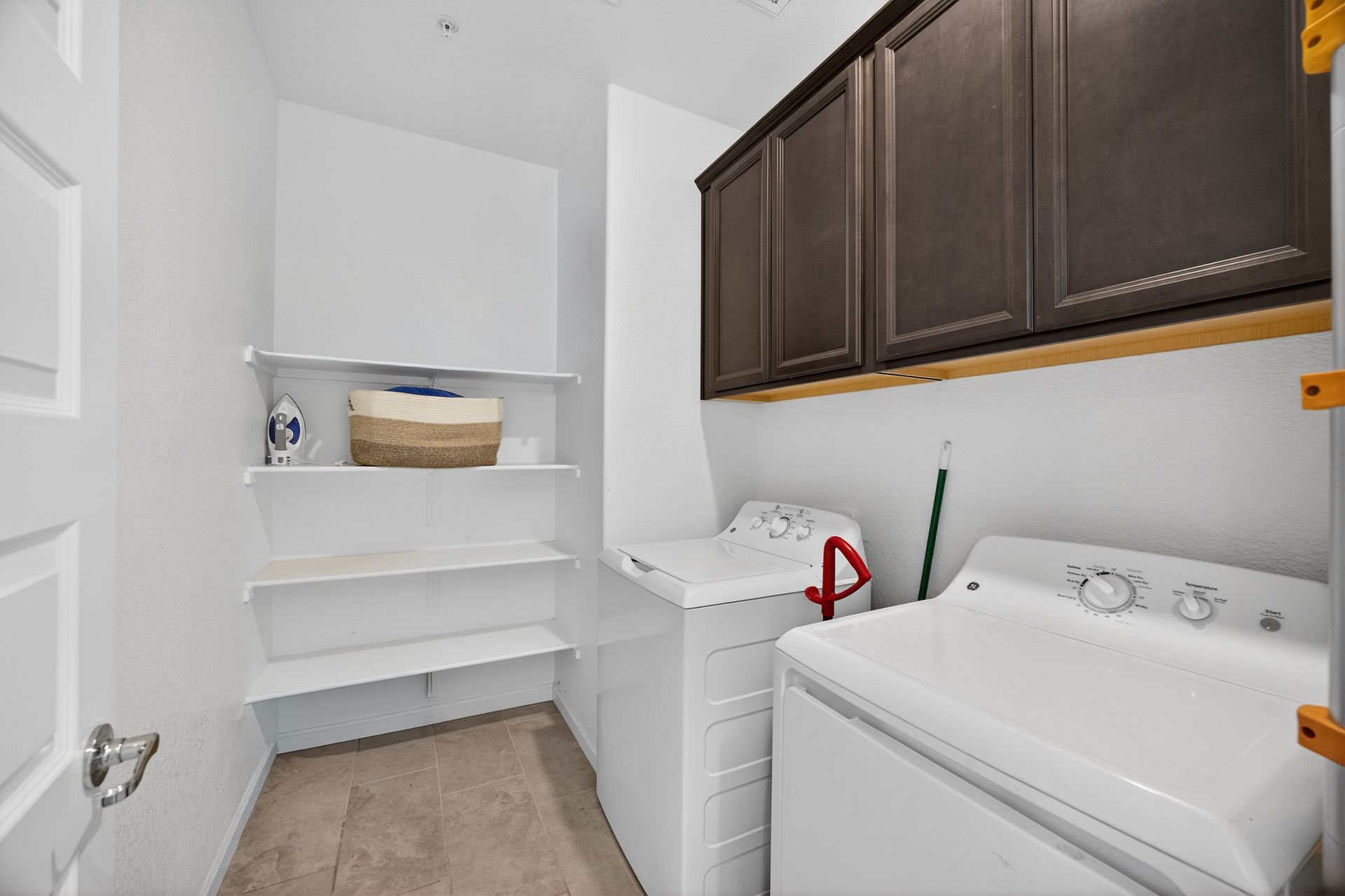Laundry room with white washer and dryer, shelves, and dark brown cabinets.