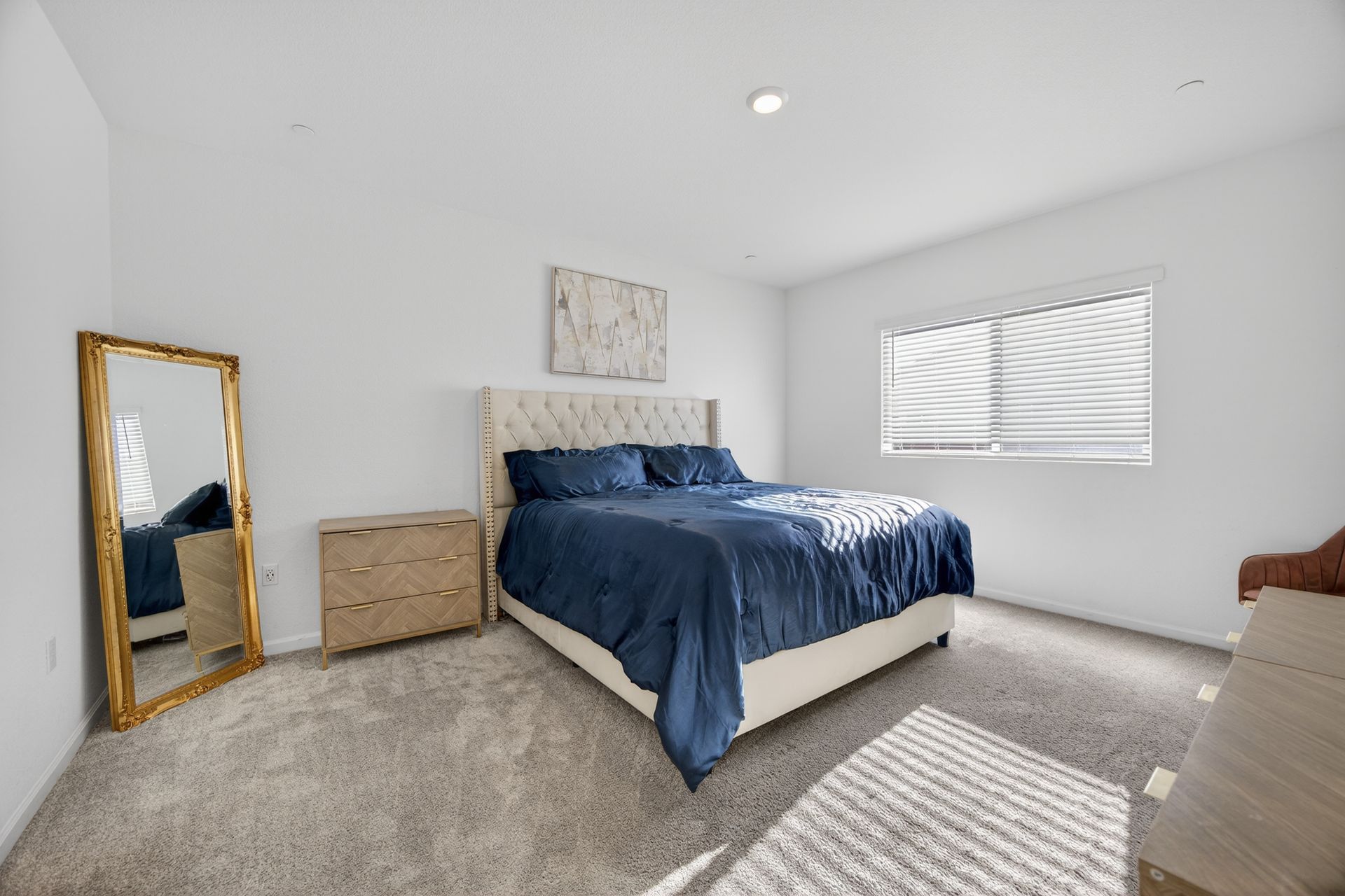 Bedroom with a bed, nightstand, mirror, and window with blinds; white walls and gray carpet.