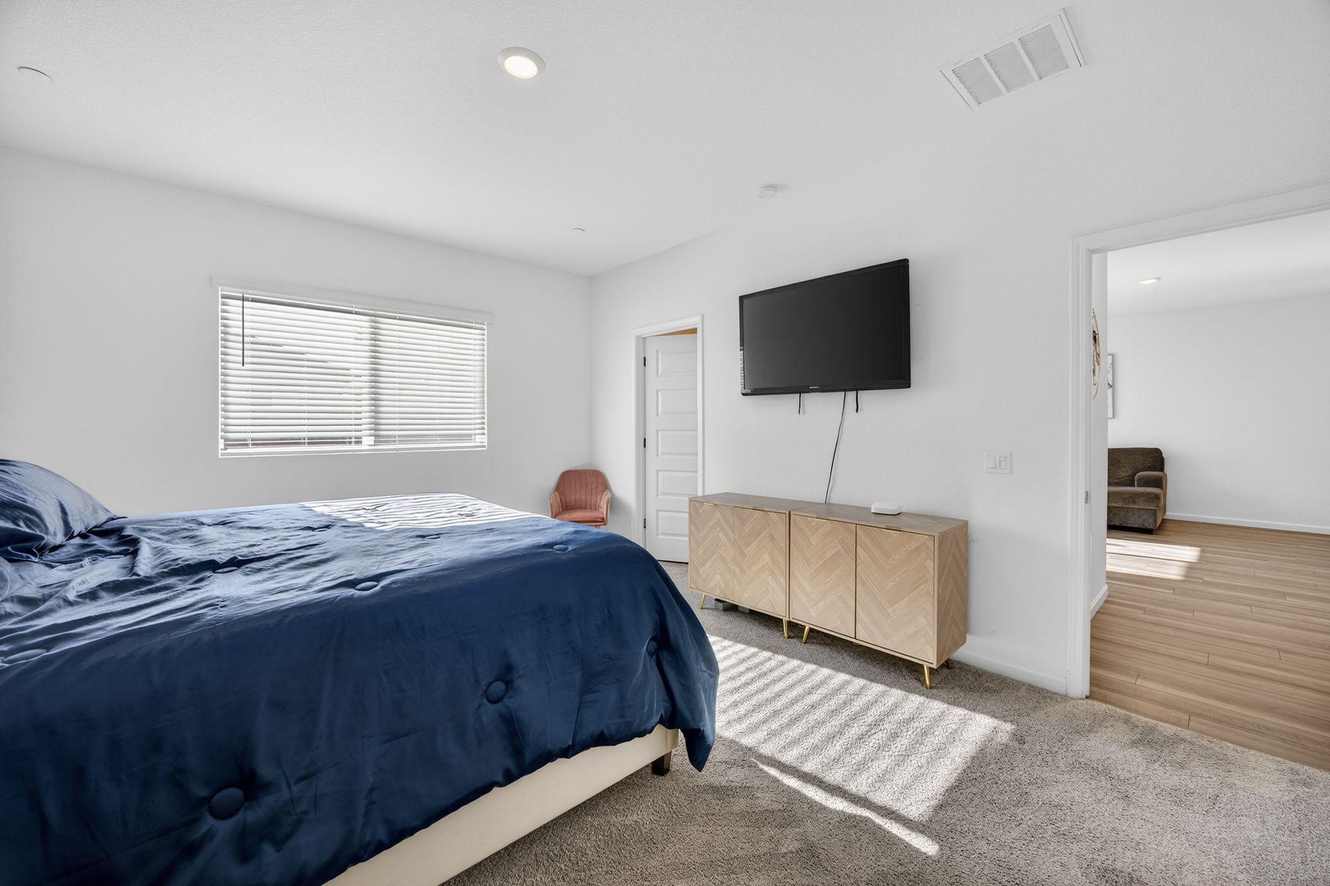 Bedroom with a blue bed, TV above a light wood cabinet, and an open doorway to another room.