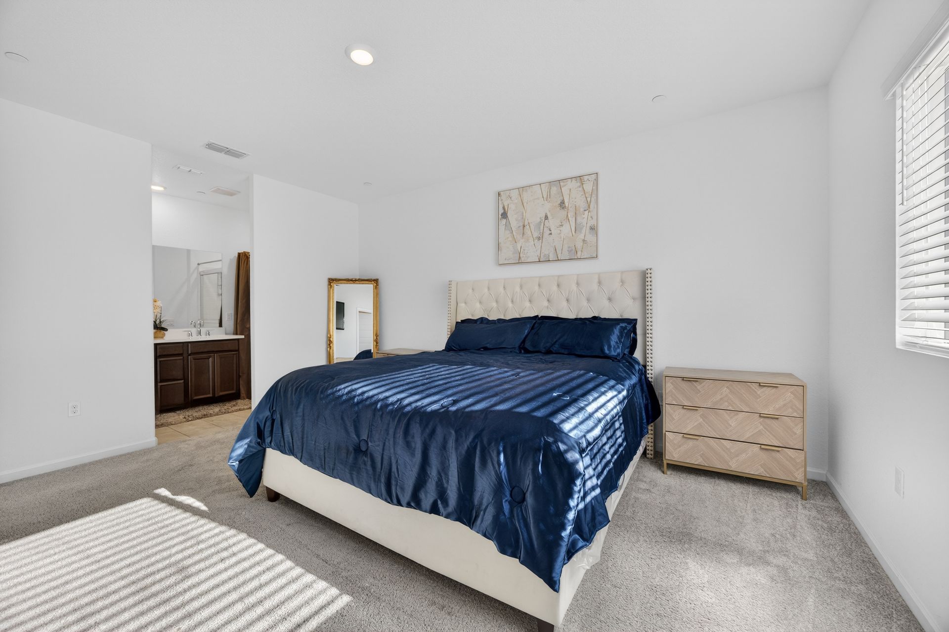 Bedroom with a large bed with blue bedding, a dresser, mirror, and access to a bathroom.