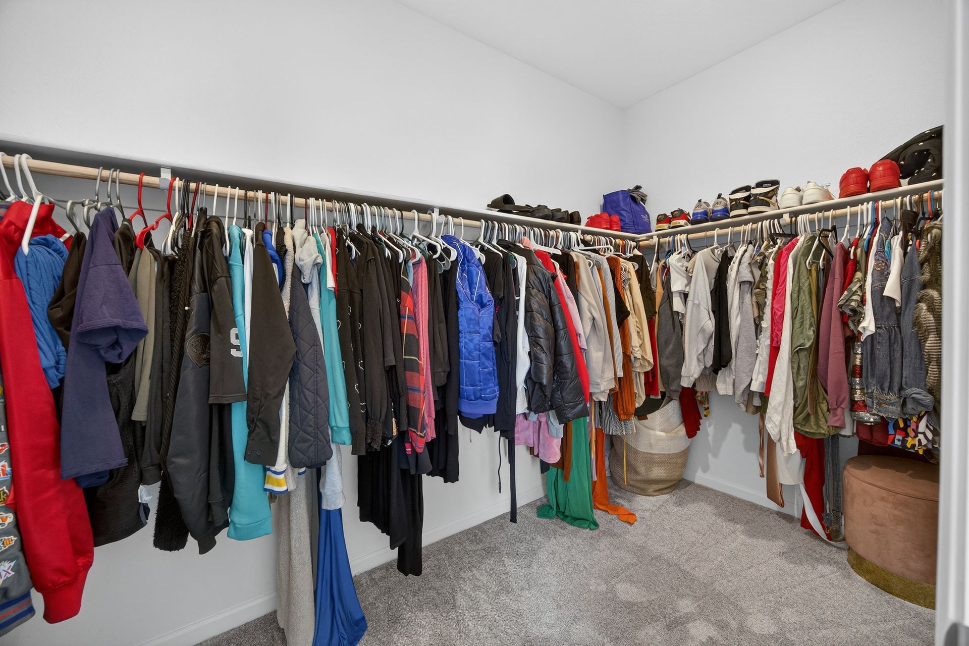 Walk-in closet with clothes hanging on racks, shoes on top shelf, and a small stool on a carpeted floor.