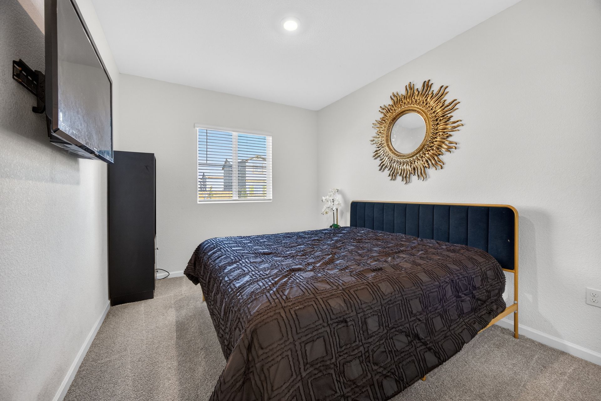 Bedroom with a bed, TV, and decorative mirror on the wall. The bed has a dark blue bedspread.