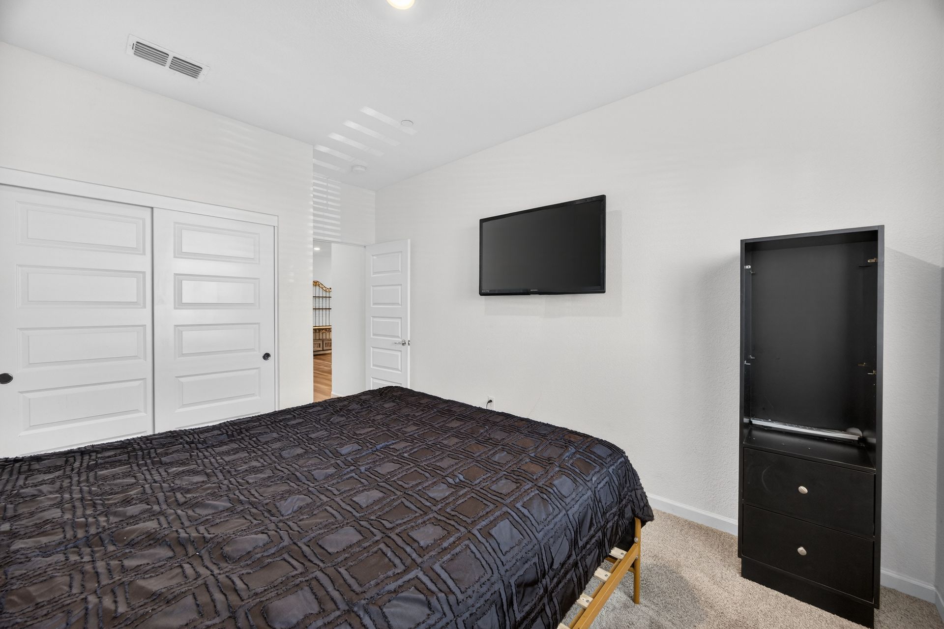 Bedroom with bed, closet, TV, and black cabinet against white walls.