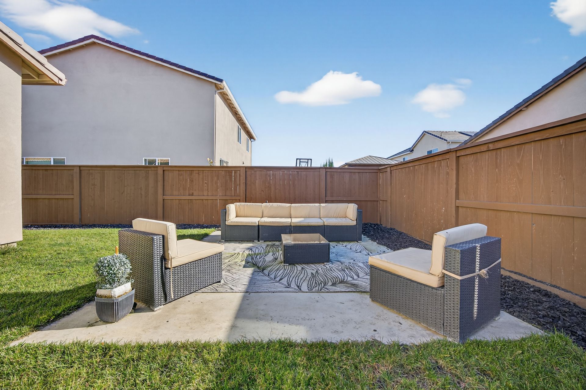 Outdoor patio with seating, wooden fence, grass, and blue sky.