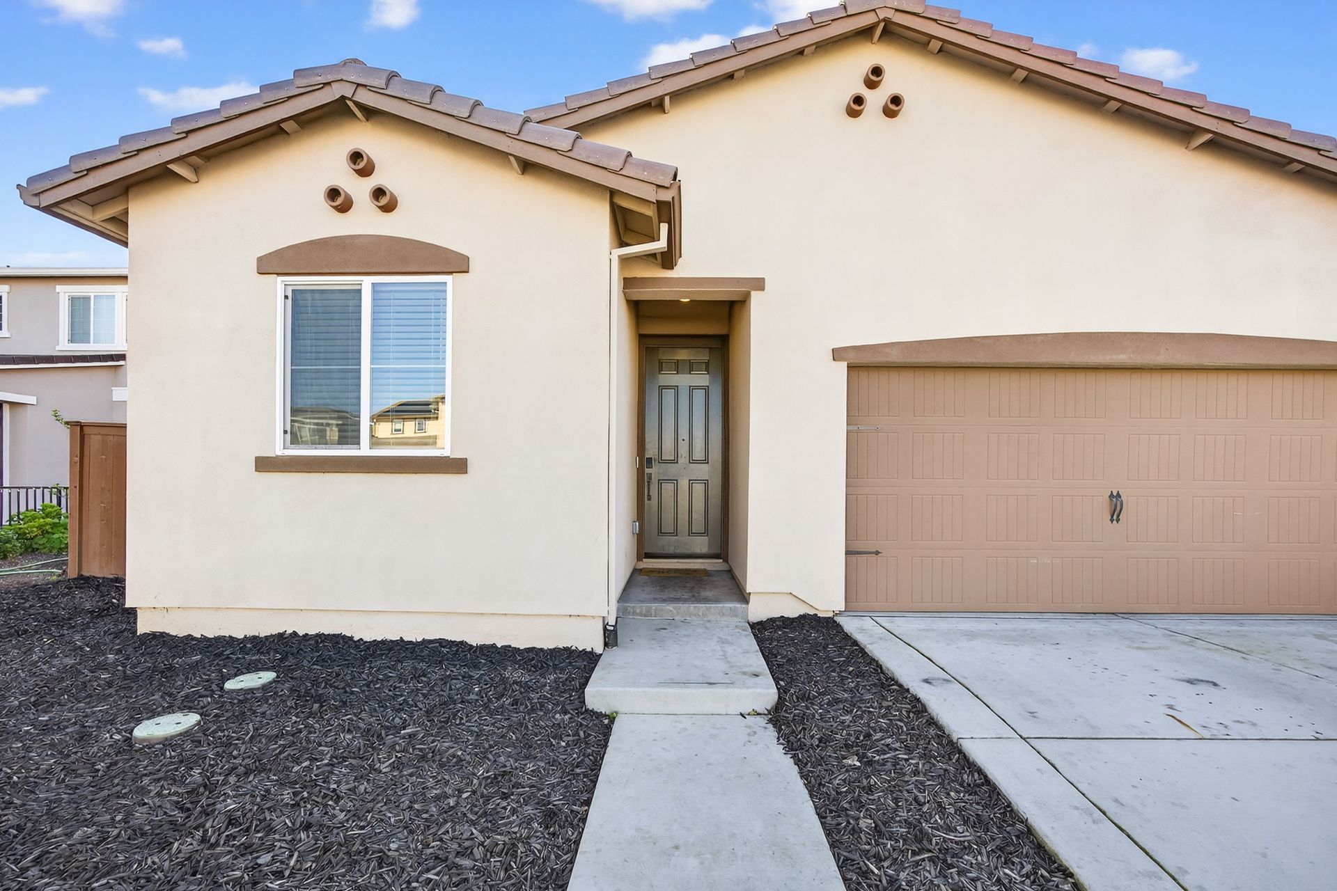 Tan single-story house with a brown roof and garage door; a concrete walkway leads to the front door.