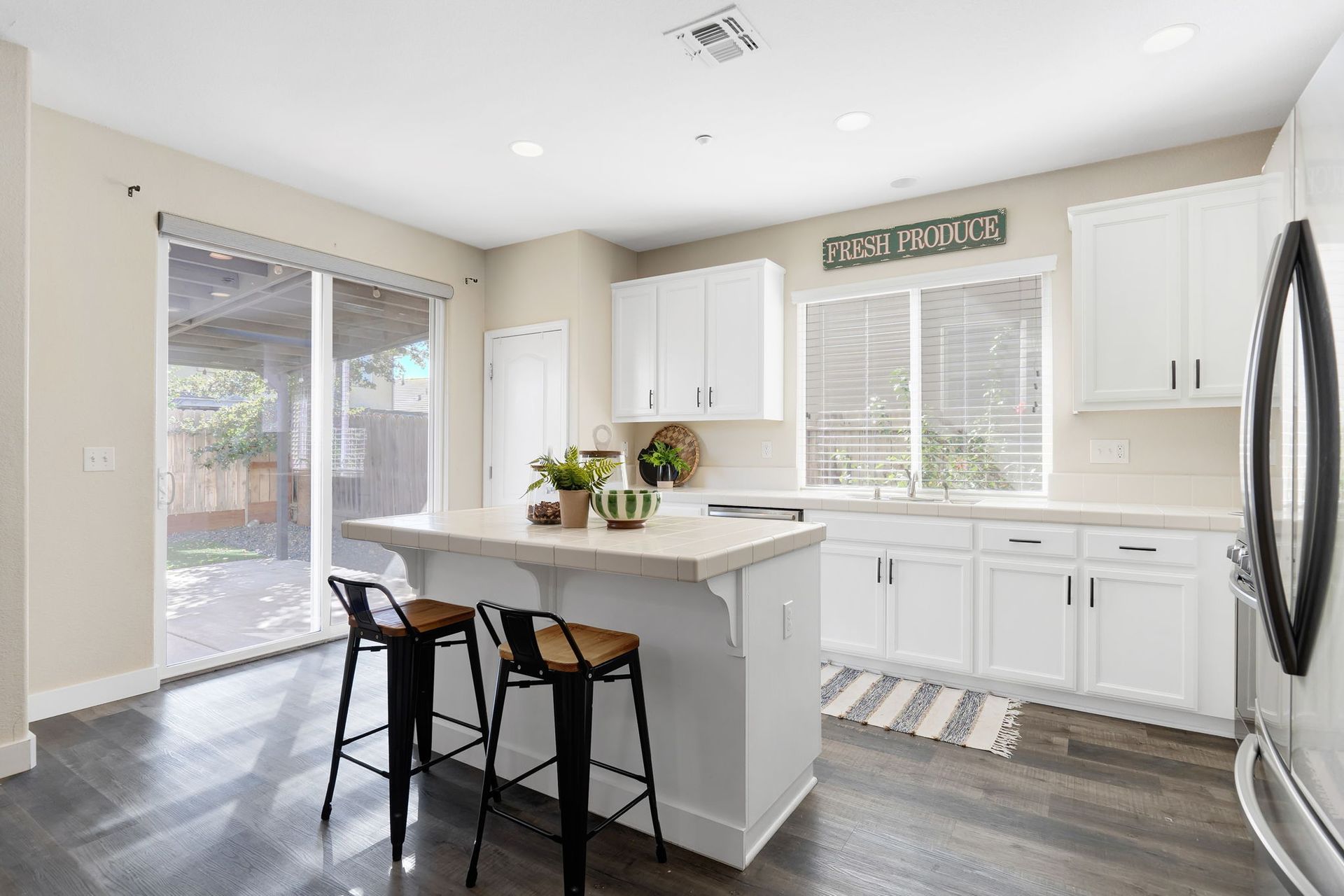 White kitchen with island, stools, cabinetry, and sliding door to backyard.