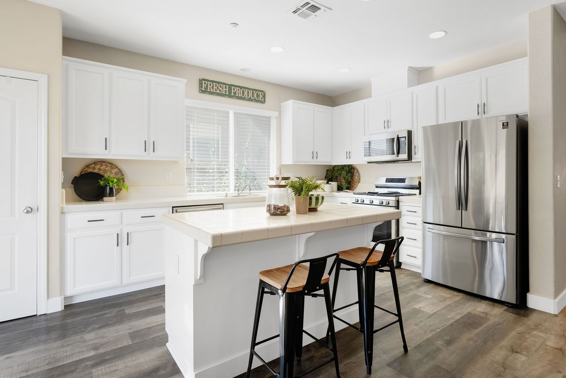 Modern kitchen with white cabinets, stainless steel appliances, island with stools.