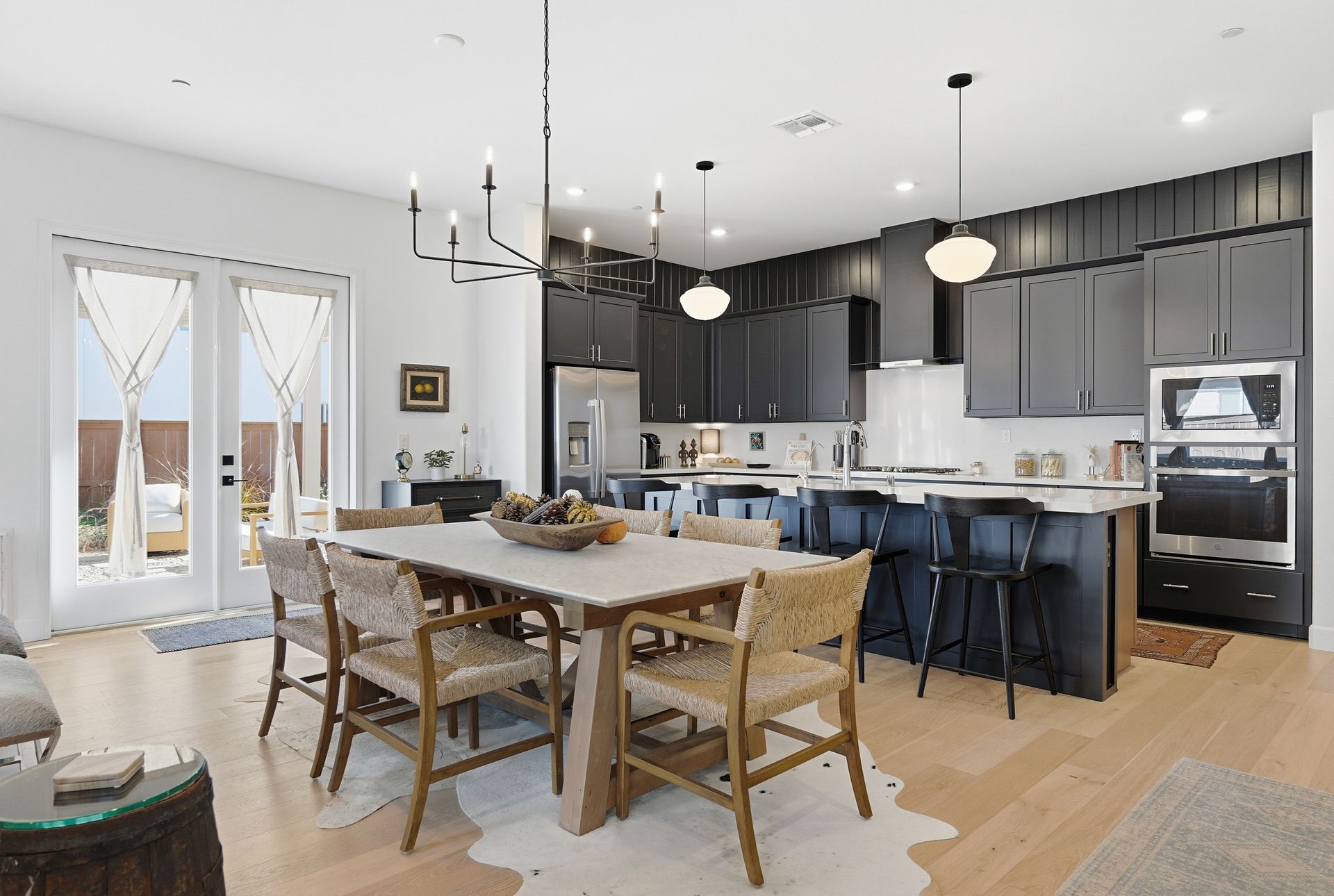 Open-concept kitchen and dining area with black cabinets, white countertops, a dining table, and french doors.