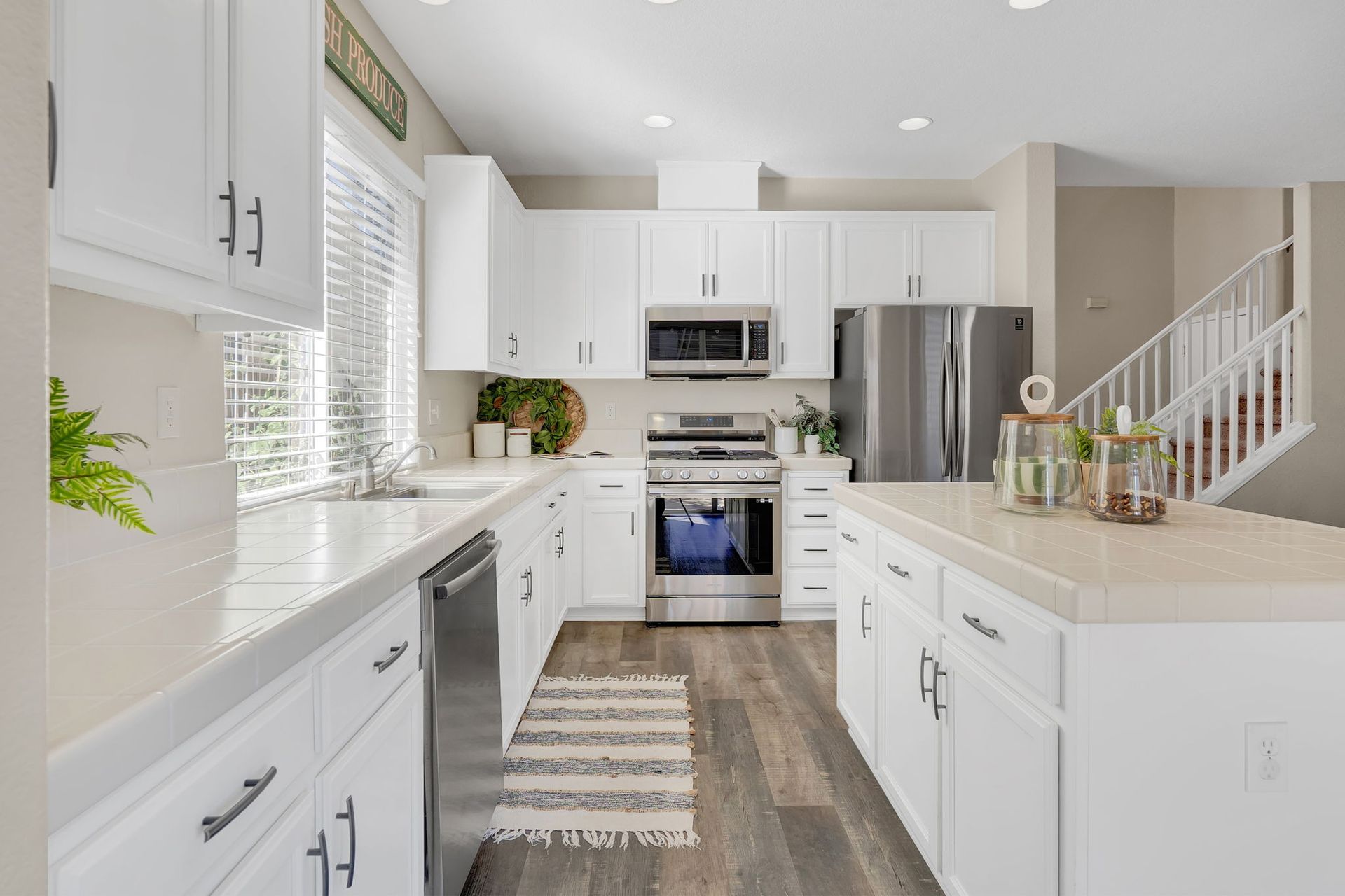 White kitchen with stainless steel appliances, white countertops, and wood-look flooring.