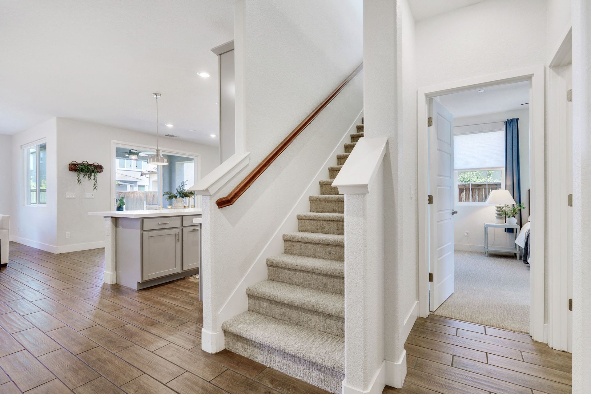 Hallway with staircase and view of kitchen and bedroom. Neutral colors: white, brown, gray.