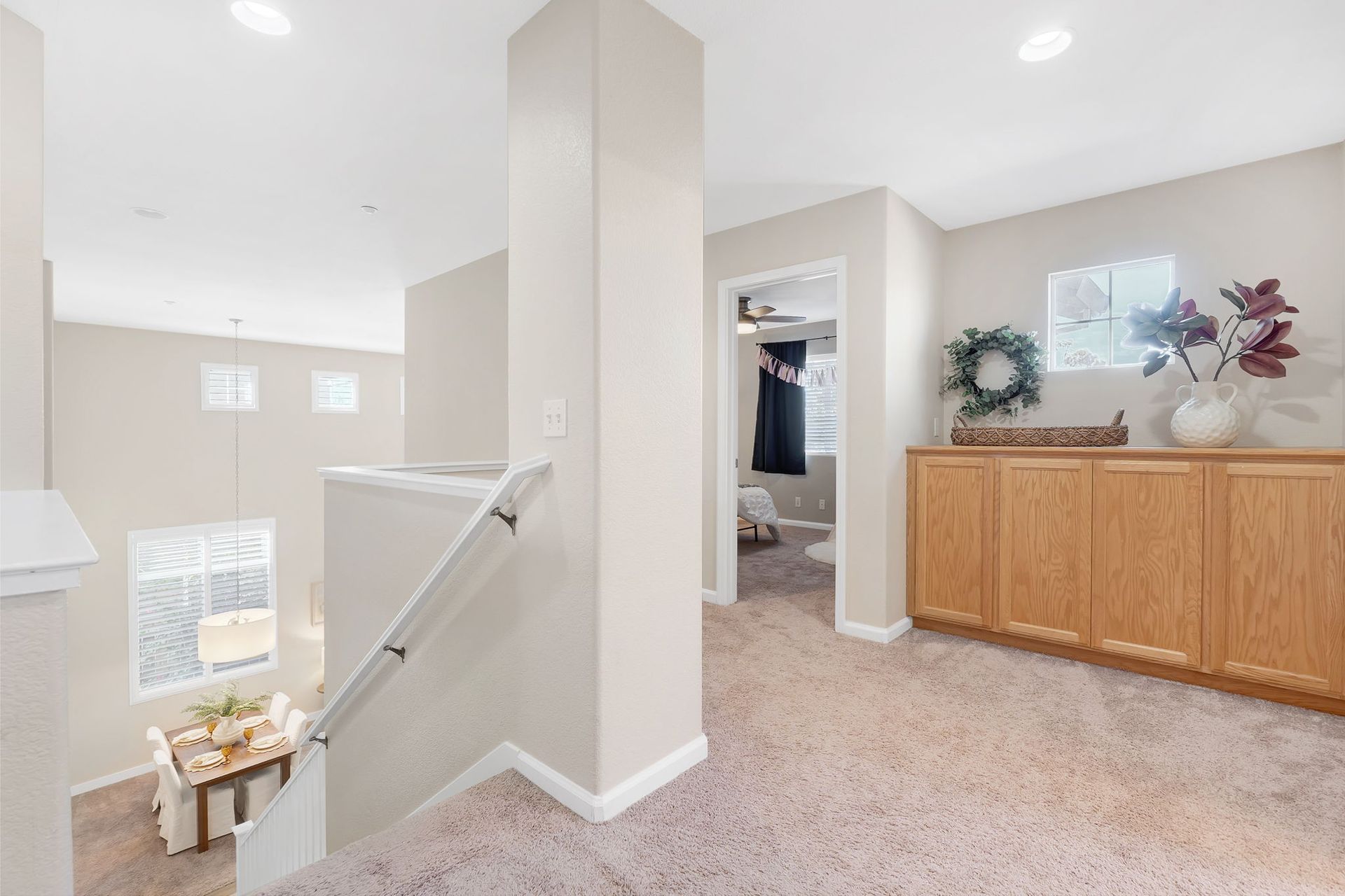 Hallway with carpet, built-in wooden cabinet, open to downstairs, and a bathroom doorway.