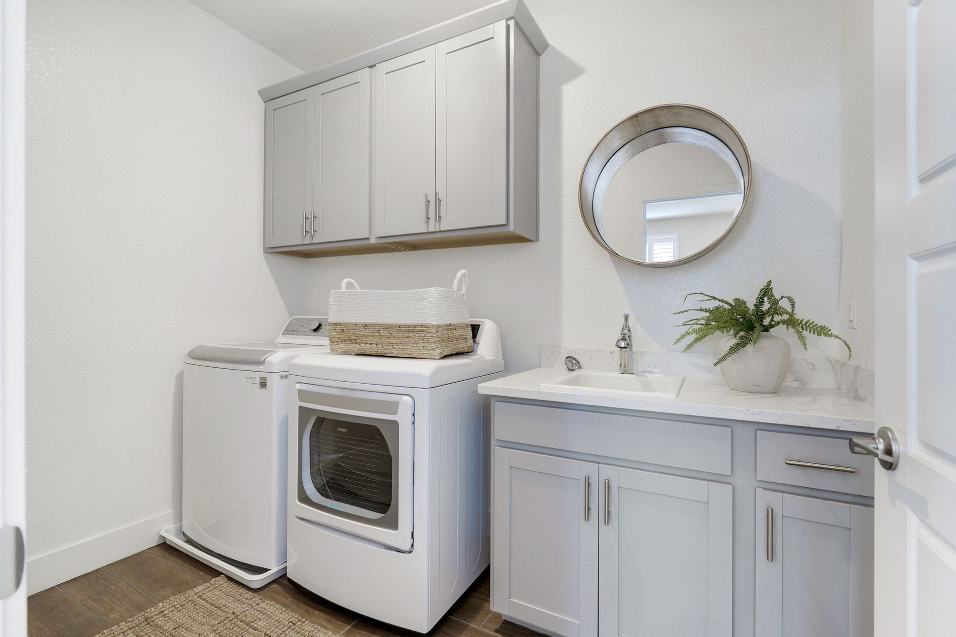 Laundry room with washer, dryer, cabinets, and a sink. Light gray cabinets, white appliances, and a round mirror.