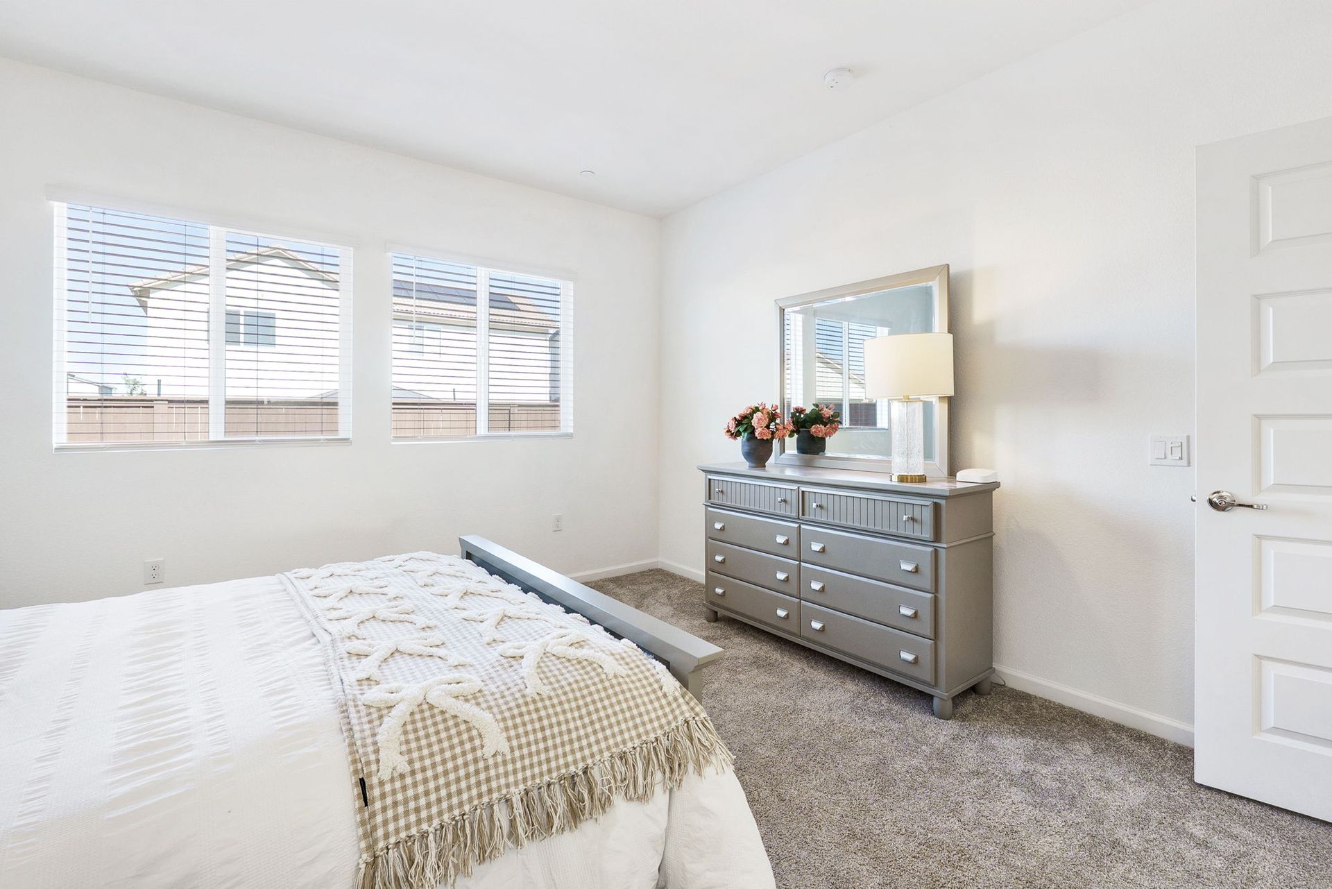 Bedroom with a bed, dresser with a mirror, and a window. Light grey walls and carpet.