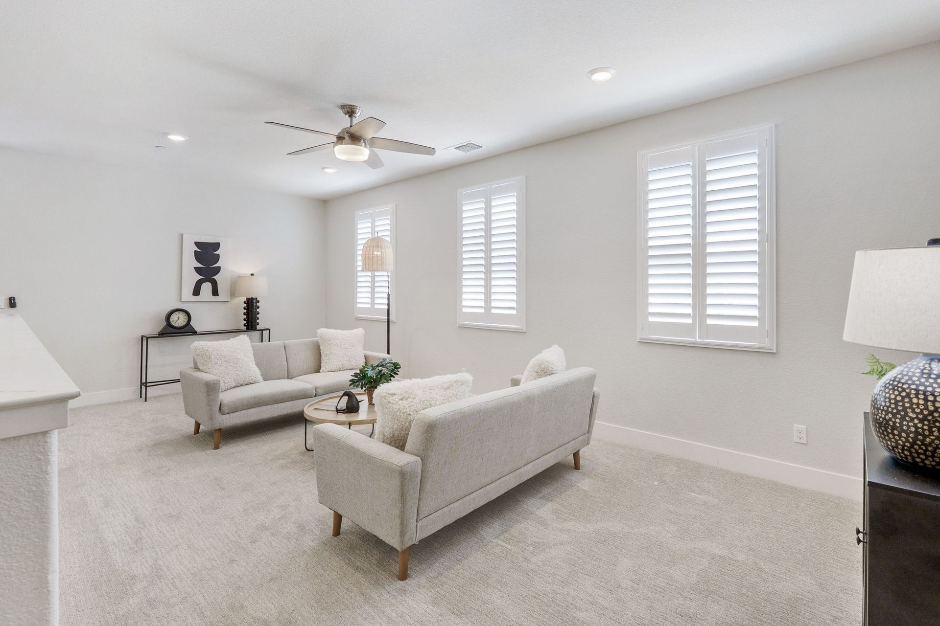 Spacious, bright living room with two couches, round coffee table, and three shuttered windows.
