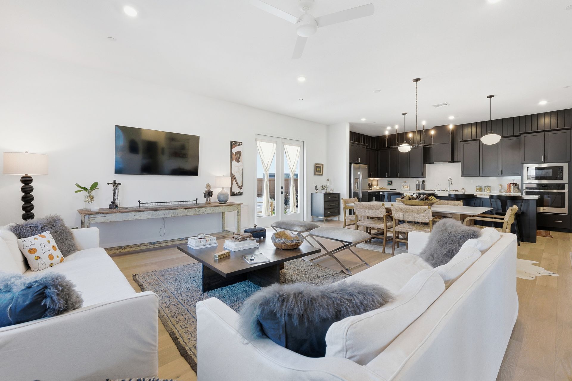 Open-concept living space with white sofas, dark kitchen cabinets, and a dining area.