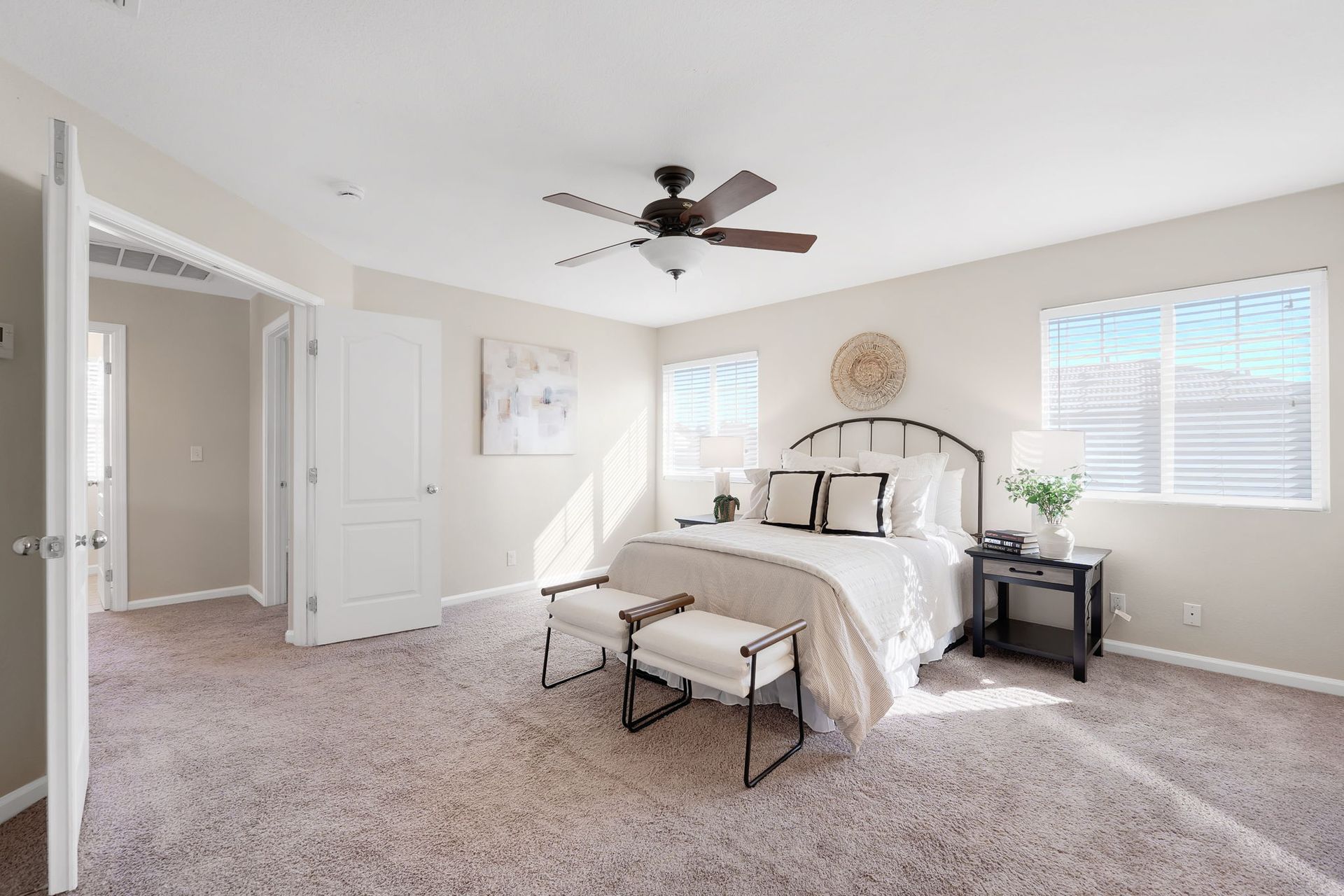 Bedroom with a bed, two ottomans, and a nightstand. Neutral colors and a ceiling fan are present.