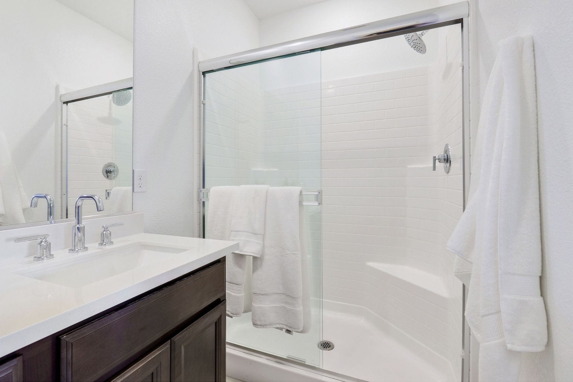 Bathroom with white shower, sink, dark cabinet, and white robe.