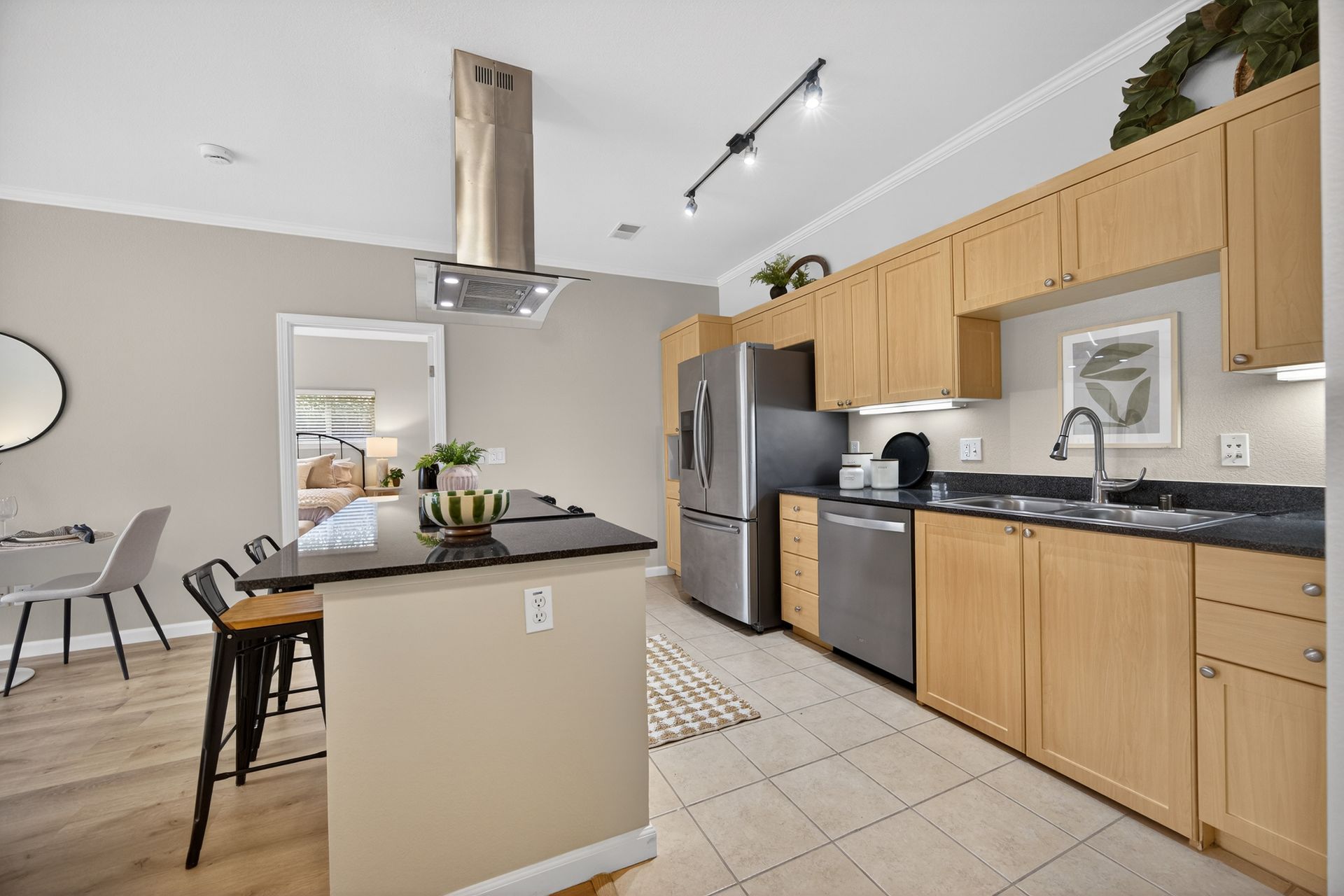 Modern kitchen with stainless steel appliances, light wood cabinets, and a black countertop island.
