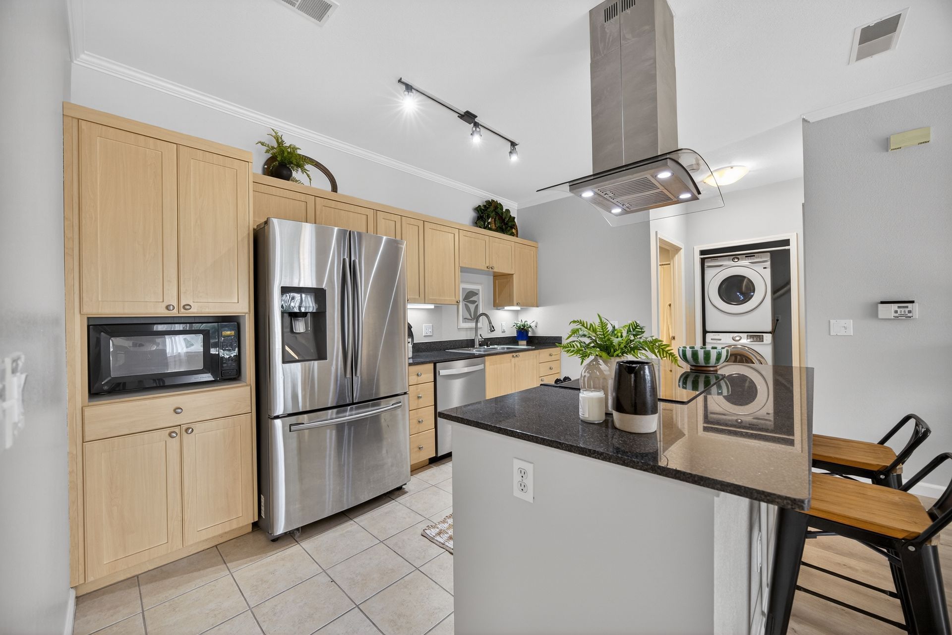 Kitchen with stainless steel appliances, light wood cabinets, and a gray island with black countertop.