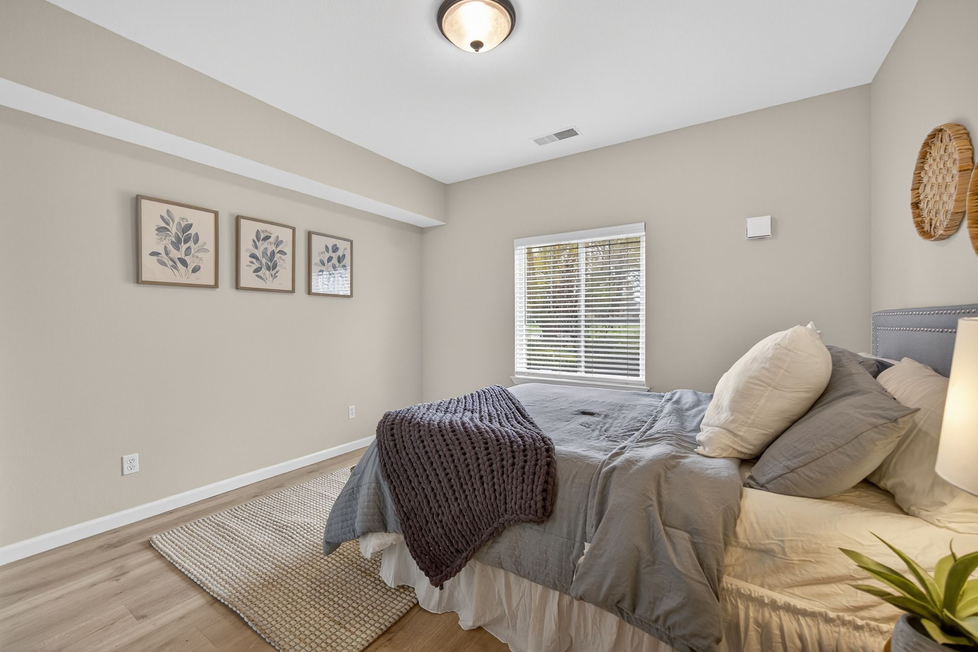 Bedroom with bed, rug, three framed pictures on the wall, and a small window.