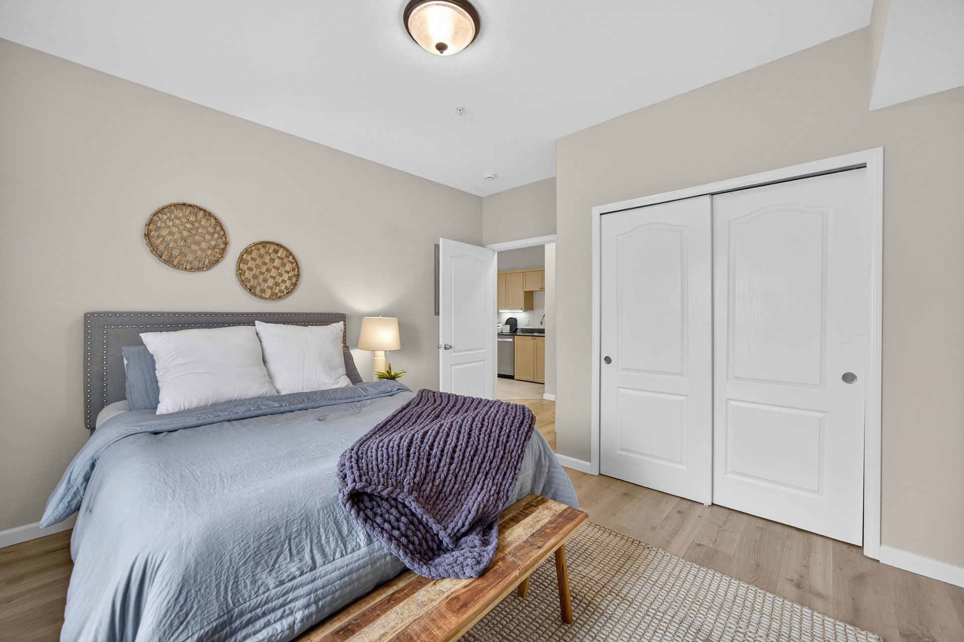 Bedroom with bed, closet, and open doorway to a kitchen; neutral tones and decorative elements.