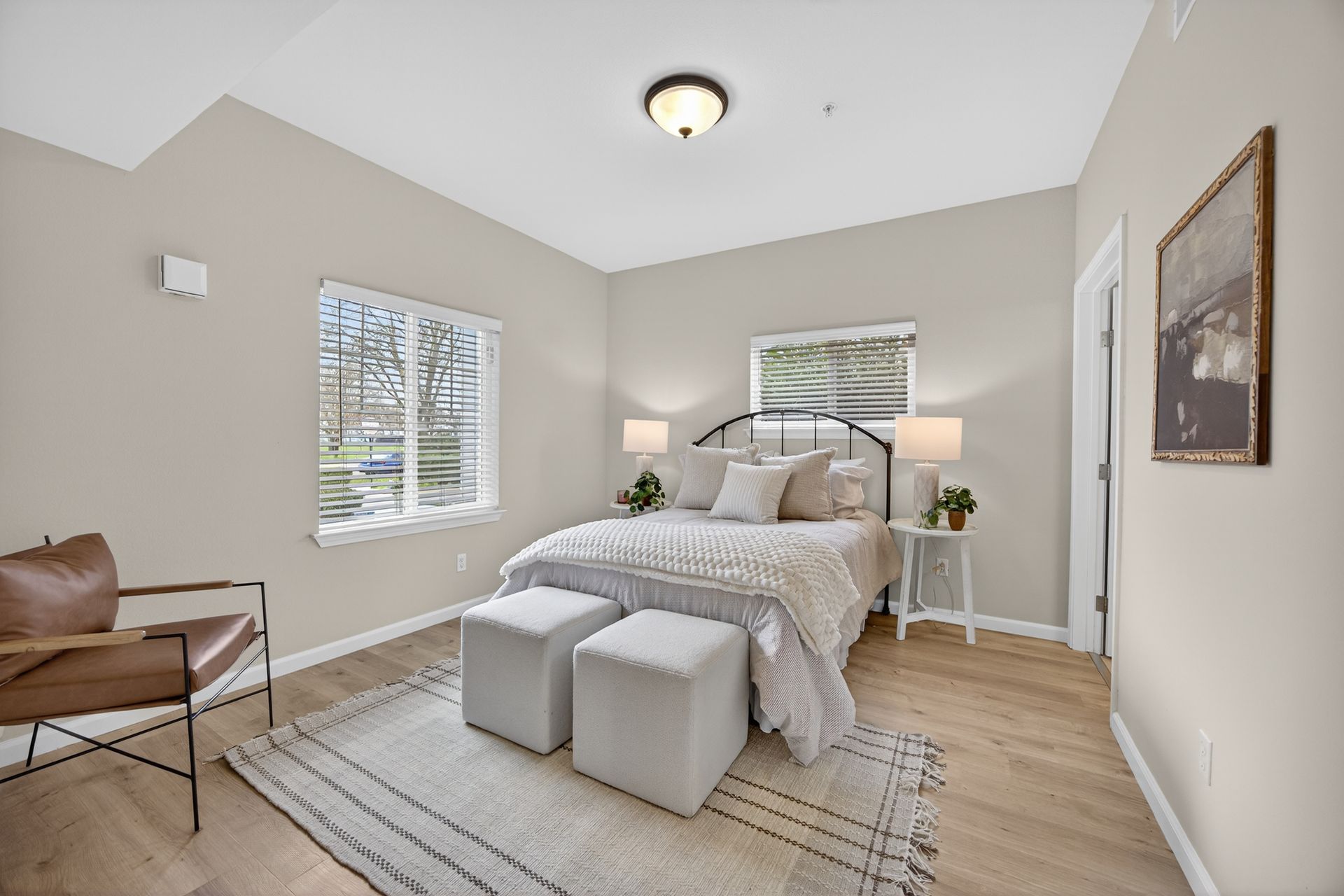 Bedroom with bed, side tables, window, rug, and leather chair.