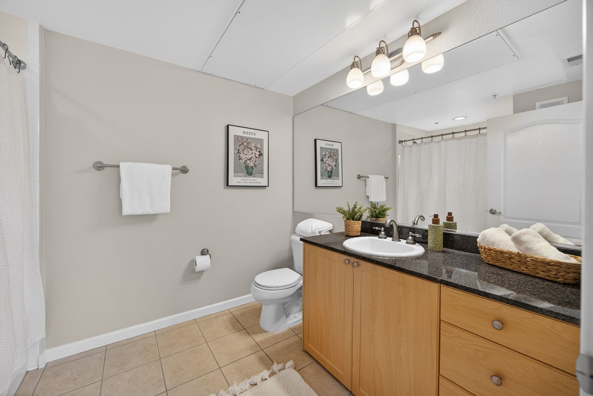 Bathroom with light tan walls, a wooden vanity, a large mirror, and a white toilet.