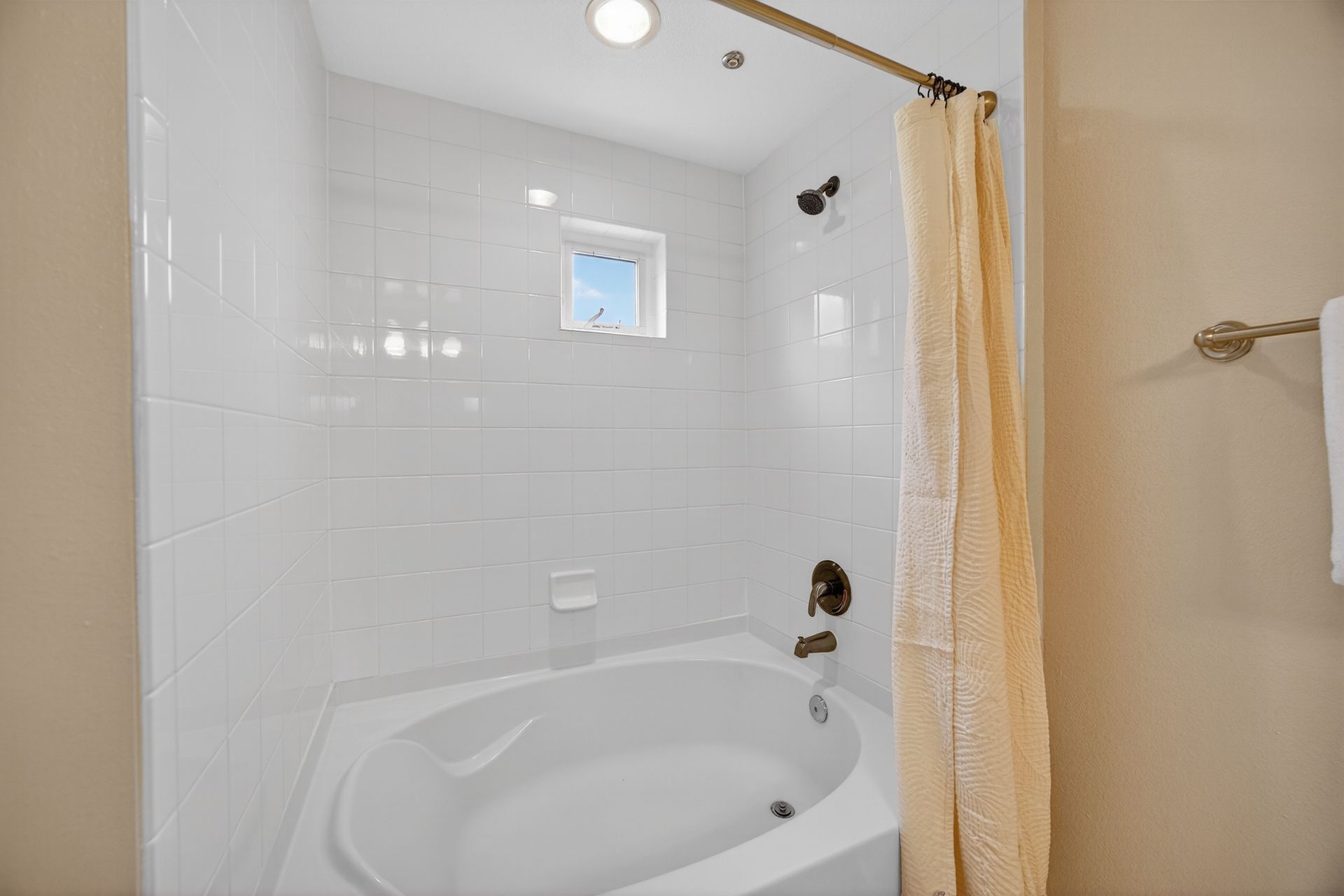 White-tiled bathroom with an oval tub and a beige shower curtain.