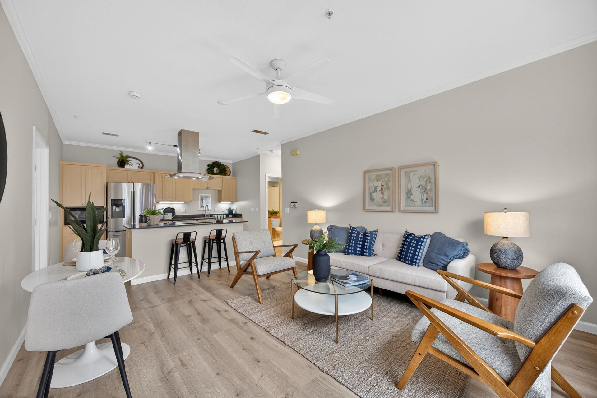 Open-plan living space with kitchen, dining, and living areas. Beige walls, wood floors, and neutral furniture.