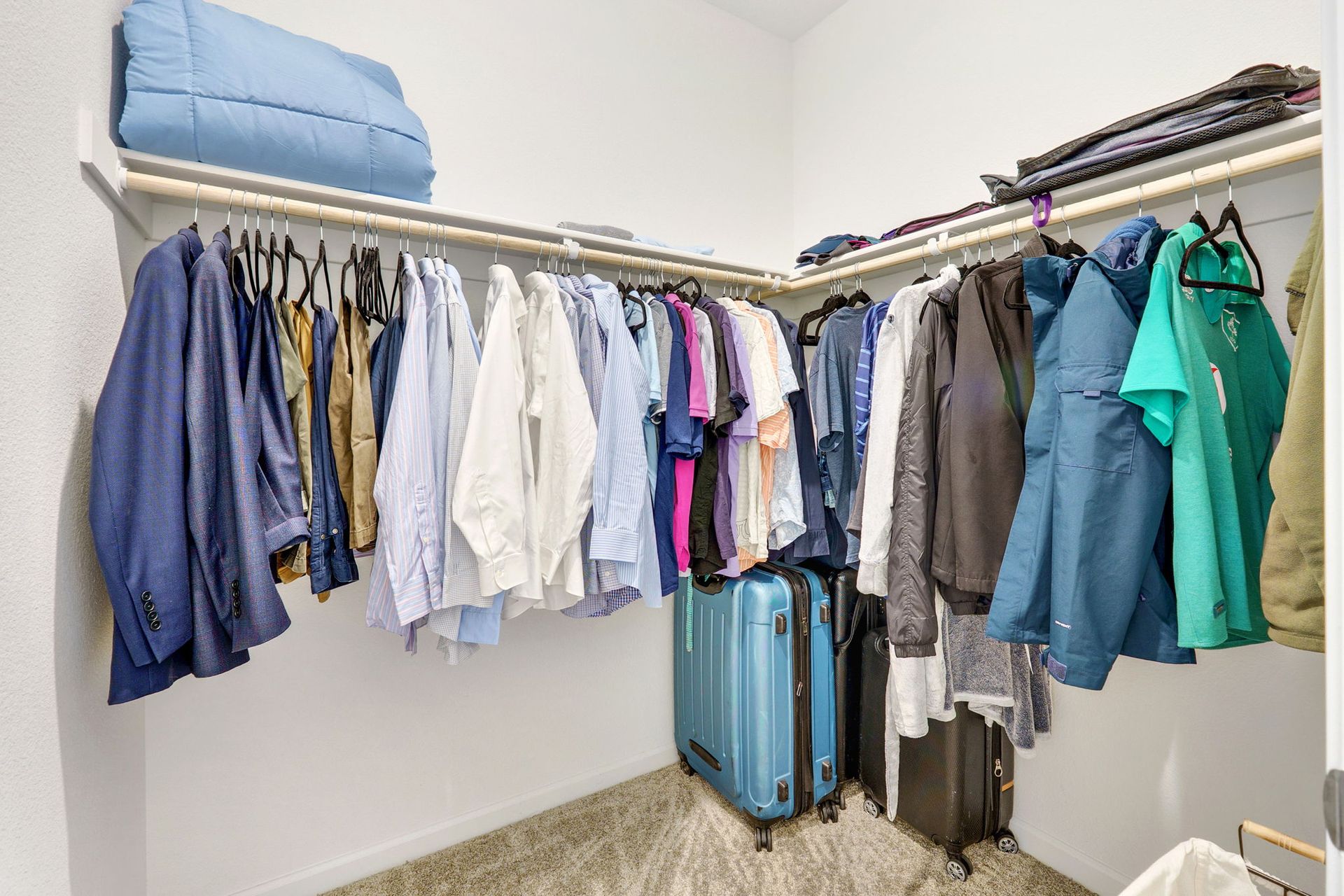 Walk-in closet with clothes hanging on rods, suitcases on the floor, and folded items on a shelf.