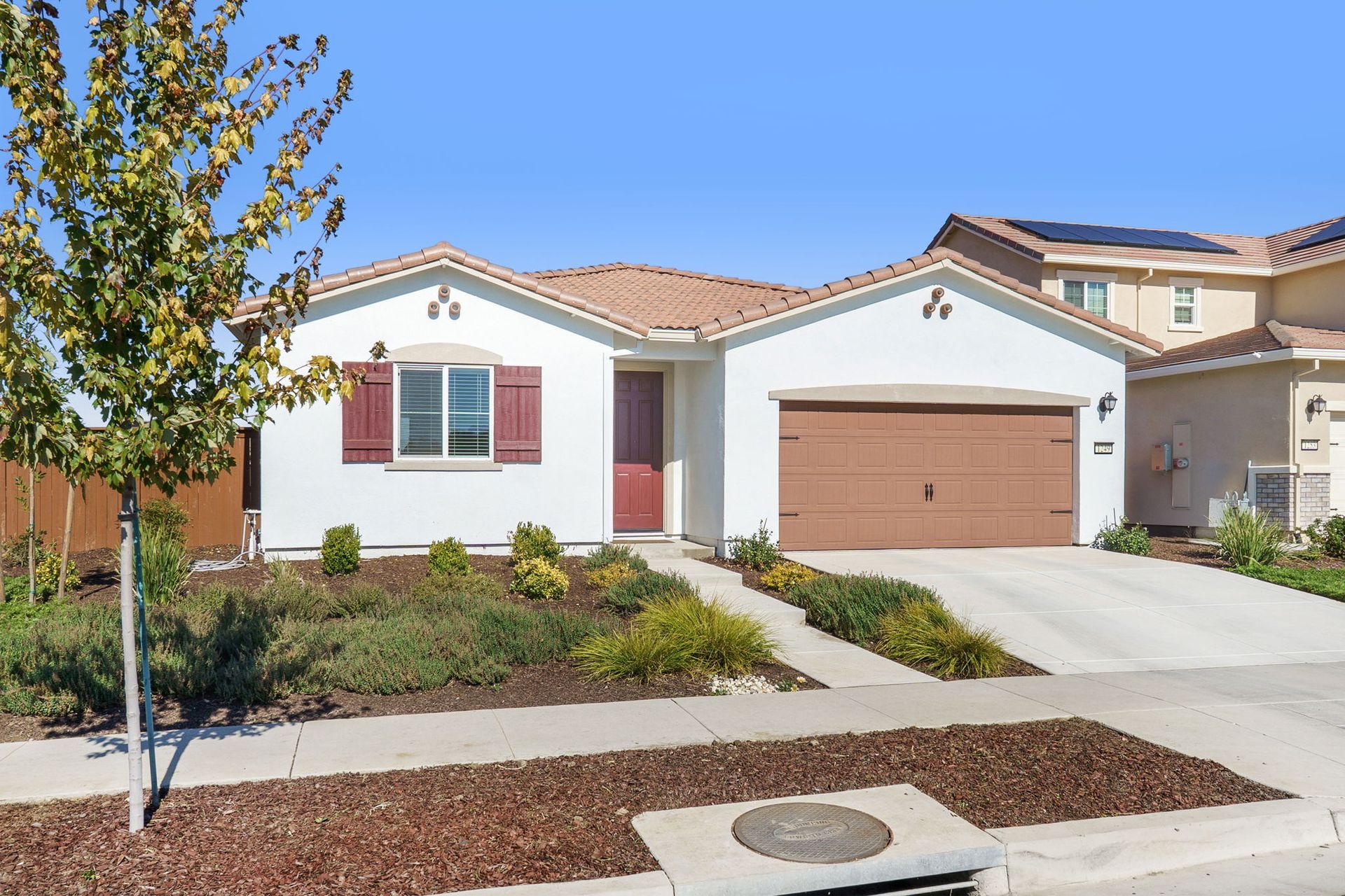 White one-story house with brown garage door, red door, and brown roof under a blue sky.