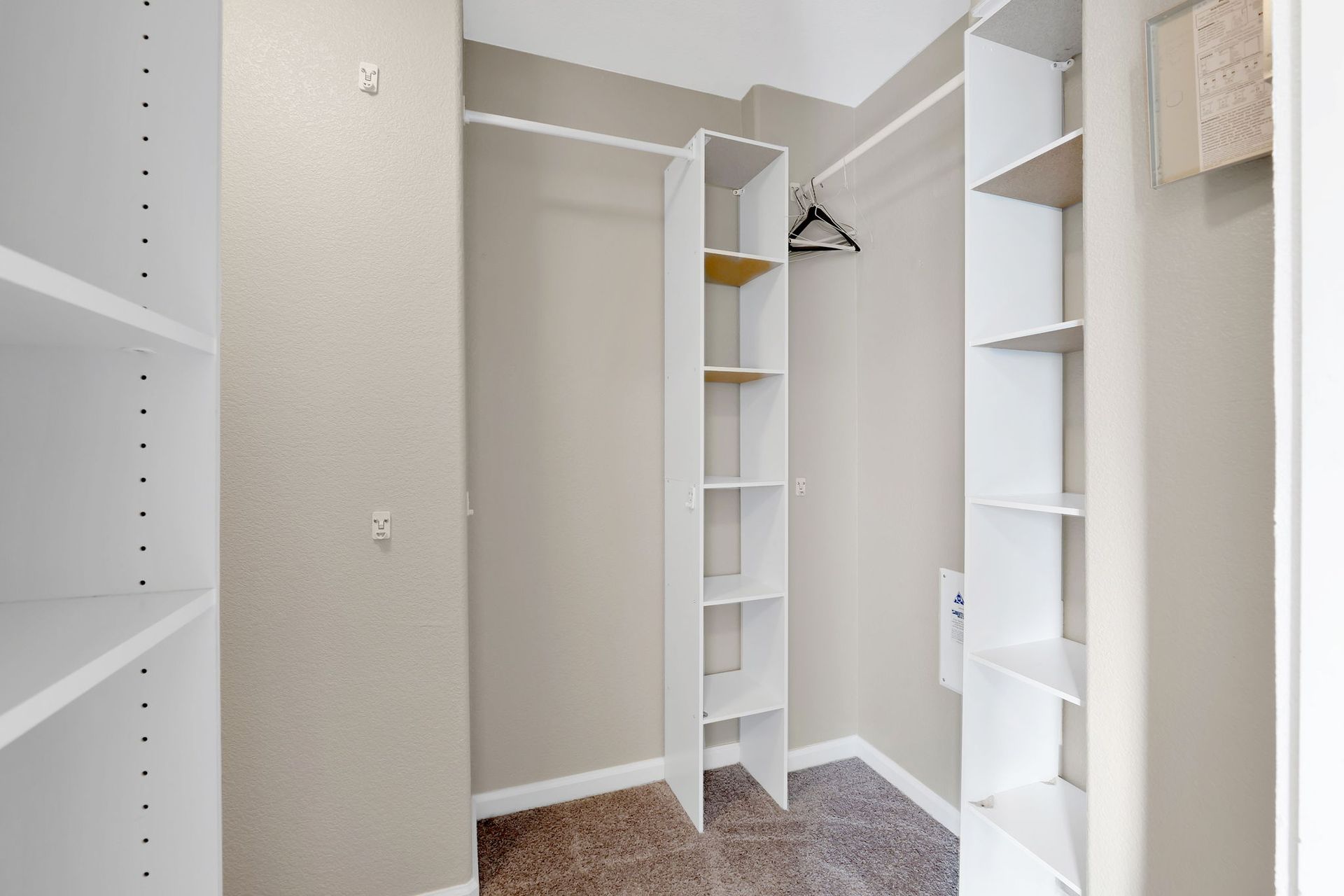 Empty walk-in closet with white shelving and neutral wall paint.
