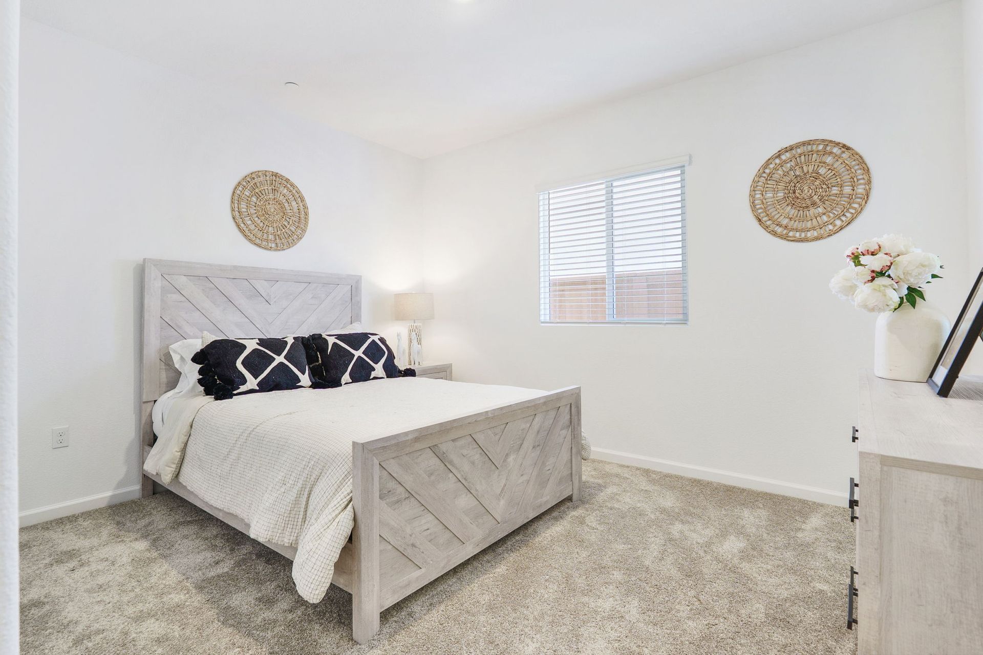 Bedroom with light wood bed, white walls, textured carpet, and decorative wall hangings.