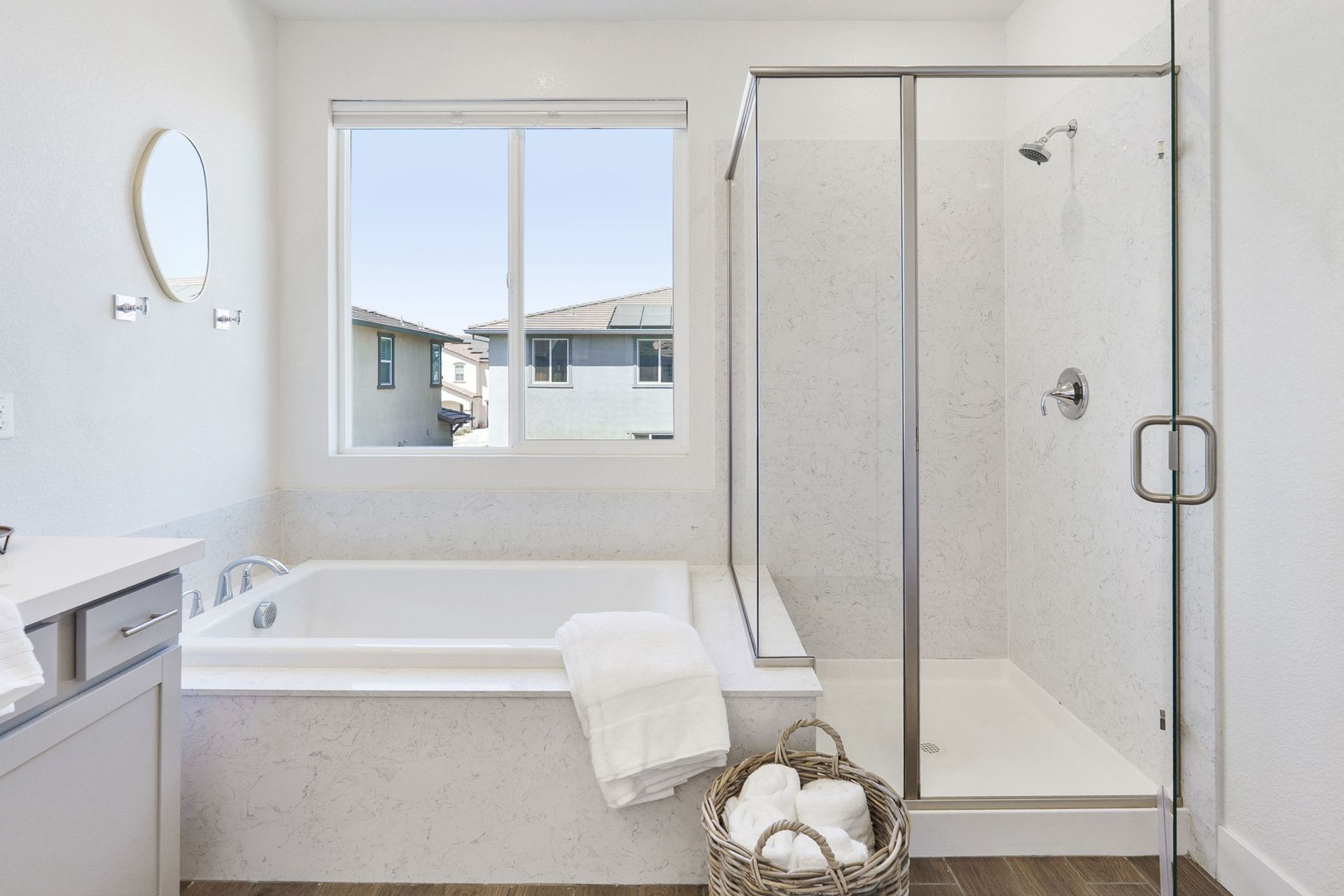 Bathroom with a white bathtub, glass shower, and window overlooking houses.