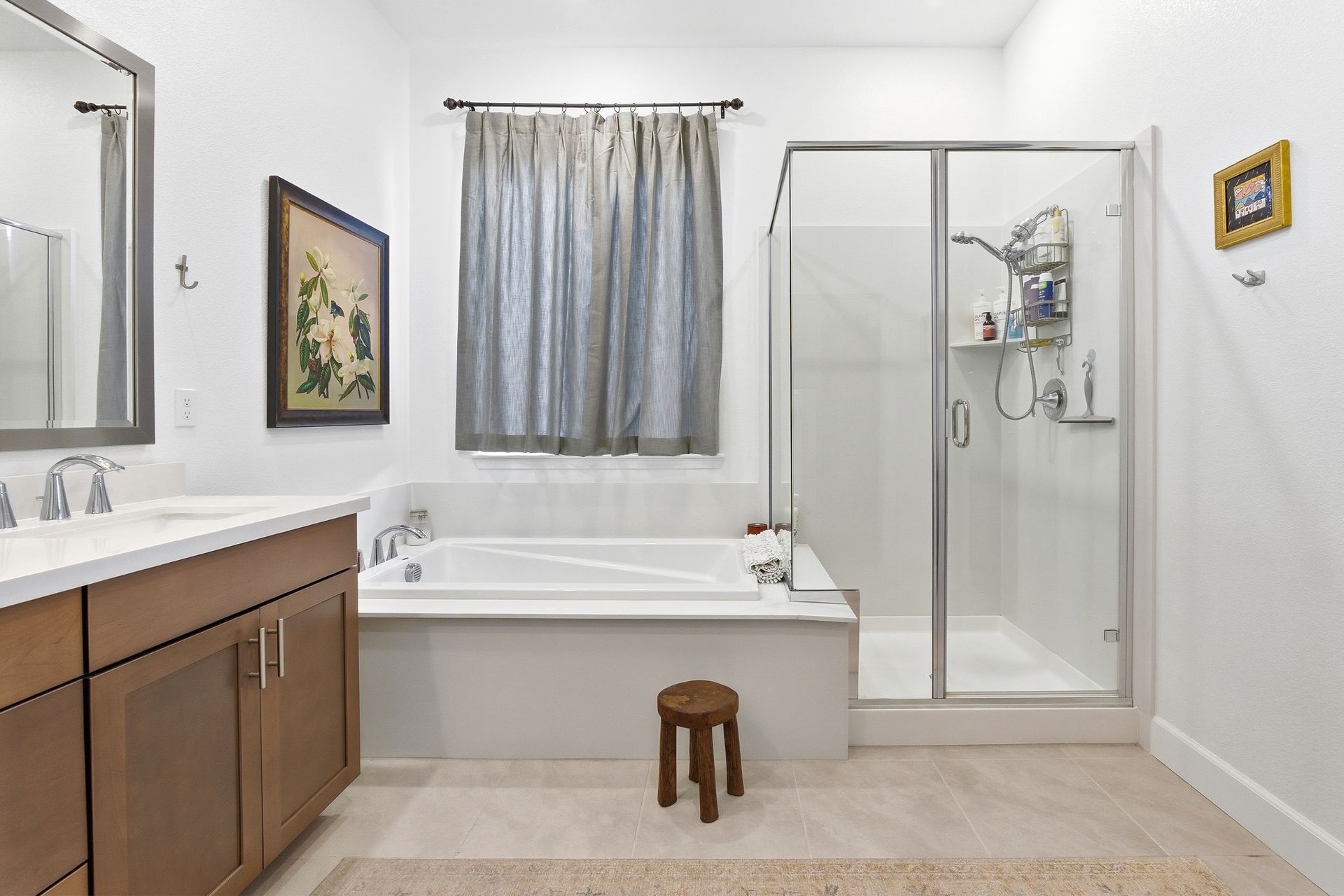 Bathroom with a bathtub, shower, vanity, and a small stool. Neutral colors and natural light.