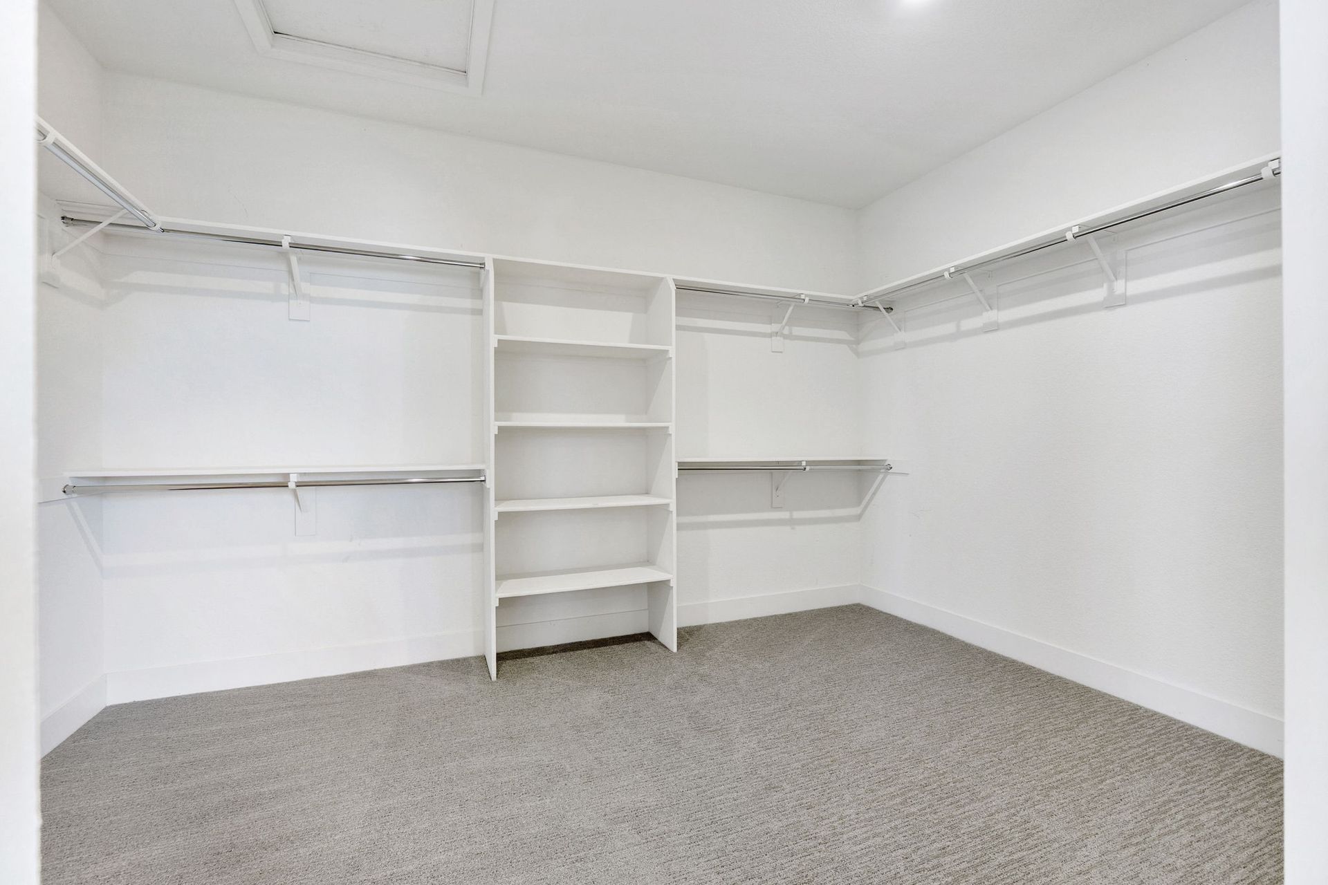 Empty walk-in closet with white walls, shelving, and gray carpet.