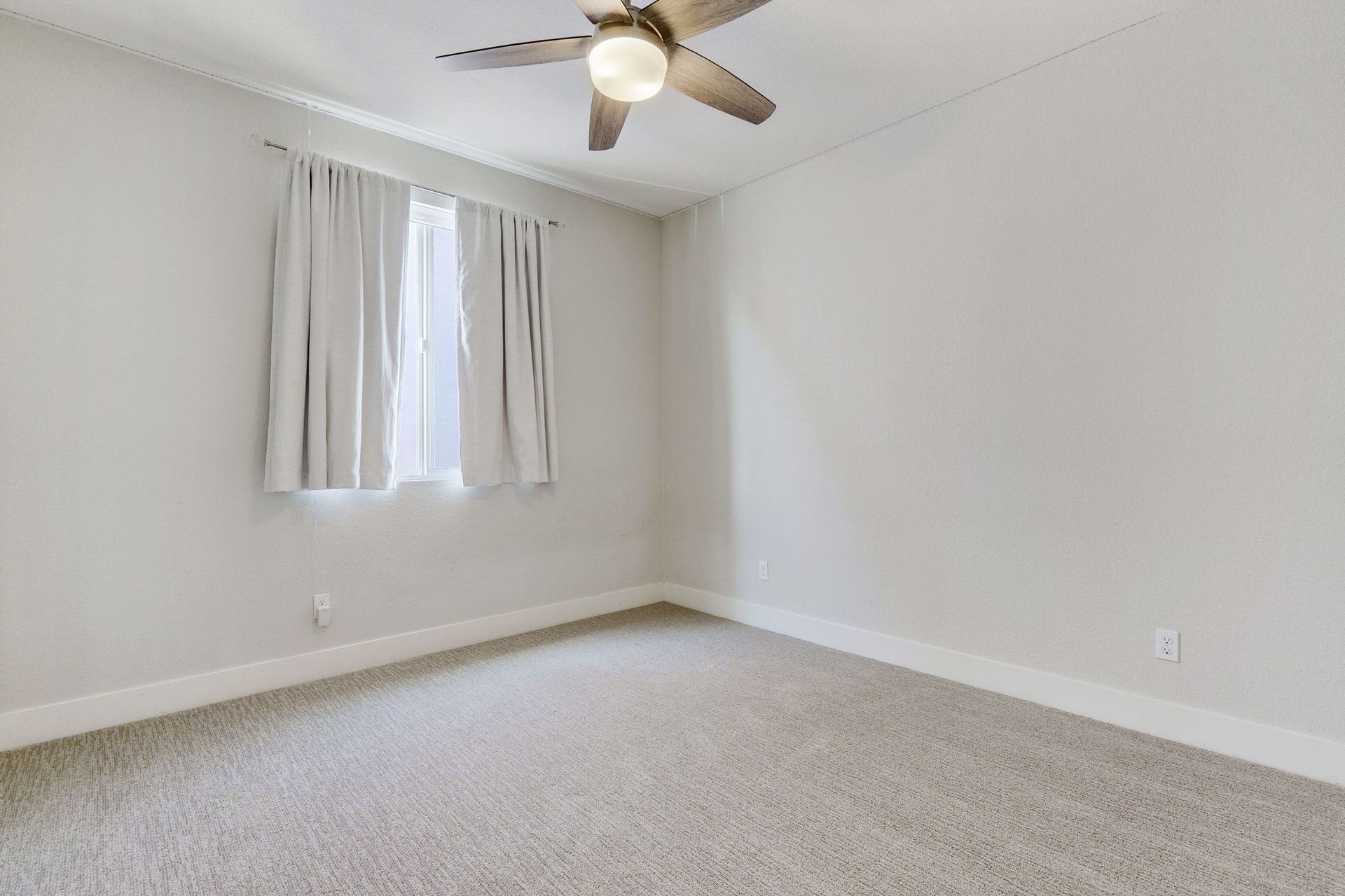 Empty bedroom with neutral walls, carpet, window, ceiling fan.